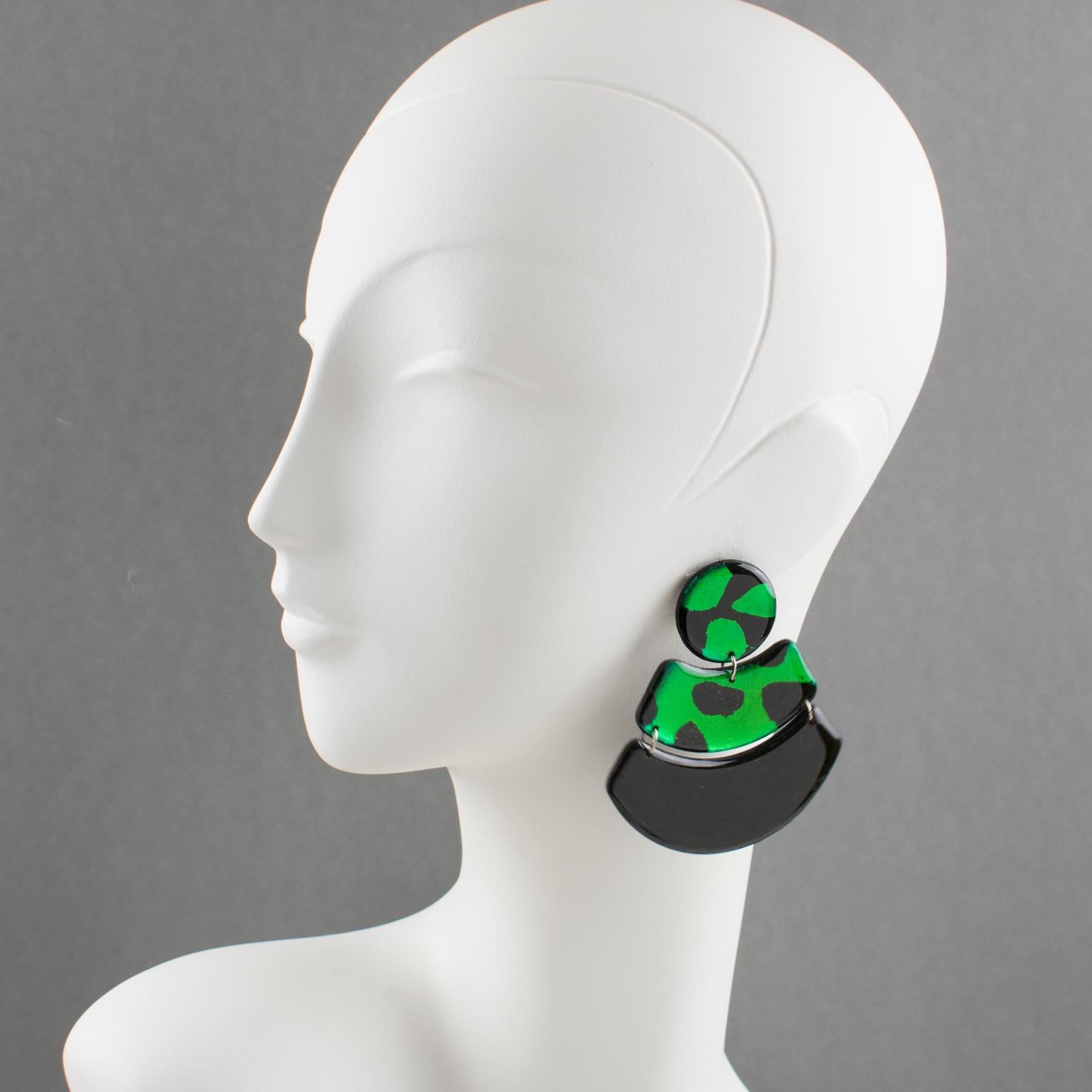 These stunning Lucite or Resin dangling resin clip-on earrings feature a massive fan shape with articulated designs. The pieces boast black and shamrock green colors. Those earrings are a total eye-catching Pop Art statement. There is no visible