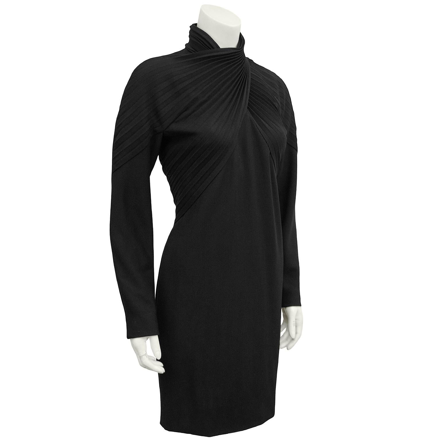 1980s black label Gianni Versace black wool cocktail dress featuring long sleeves and a turtle neckline. Beautiful pleating details at the bust that cross and wrap around the neck, creating a turtleneck. Hits above the knee. Zipper closure up centre
