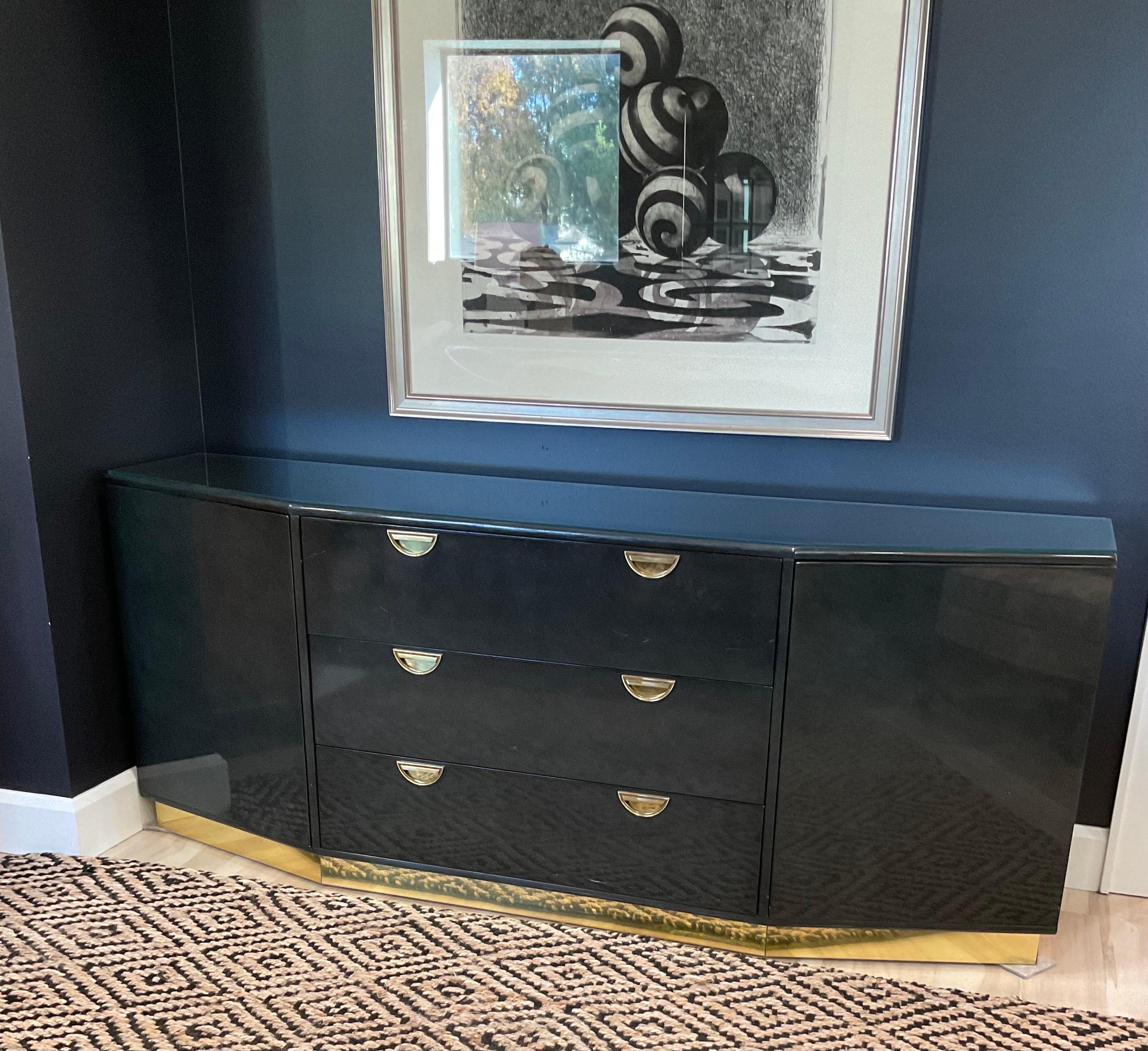 Llamativa Credenza de esquina afeitada en laca negra ahumada con espectaculares herrajes de latón y base de latón empotrada en el zócalo, de John Widdicomb. Incluso el interior de los cajones es precioso en esta pieza ultra rara. Tapa protectora de