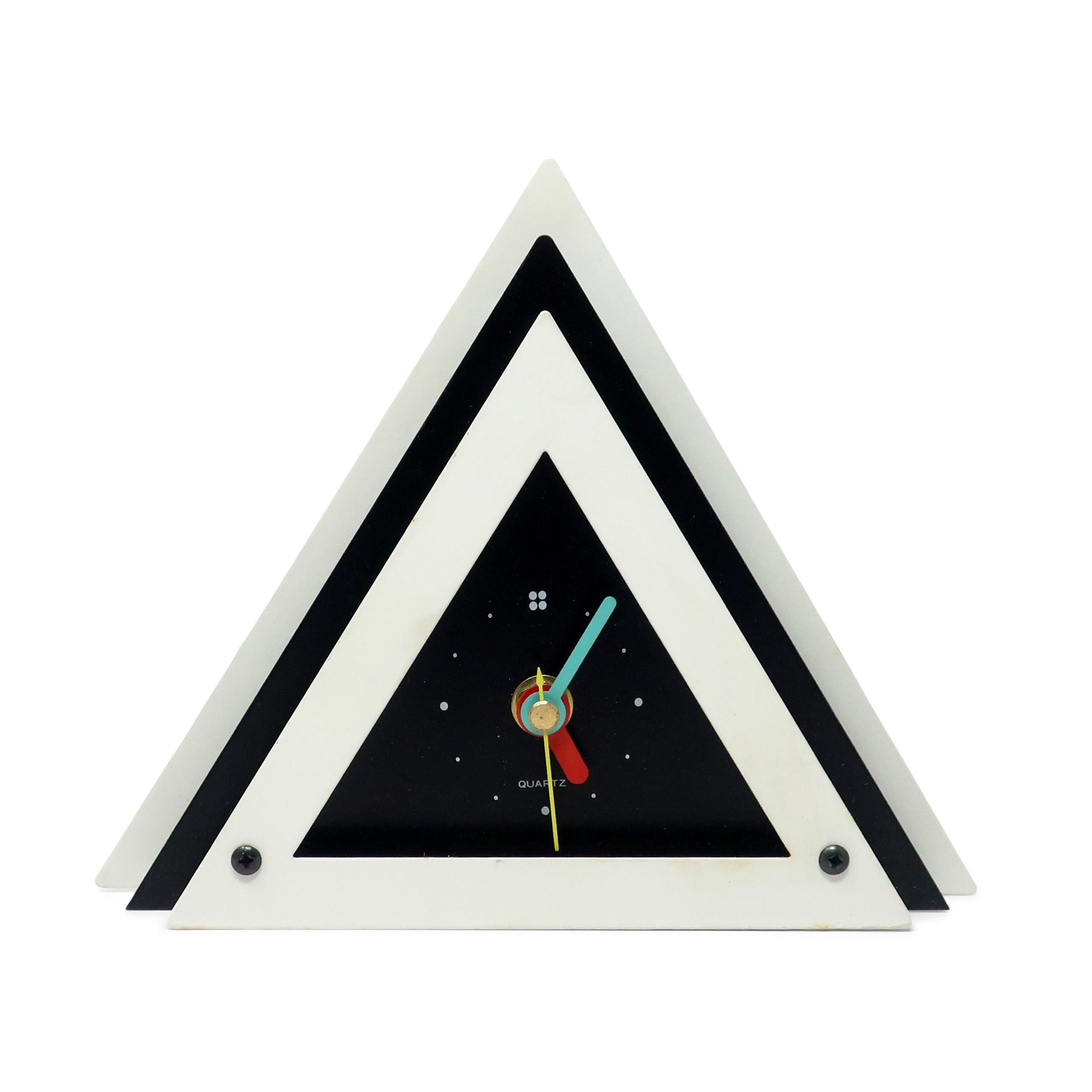 With a perfect contrast of white and black enameled metal, black lucite accents, and primary colored hands, this postmodern clock is designed with a stacked trianglular design that gives it a rare and beautiful three dimensionality.  Bold