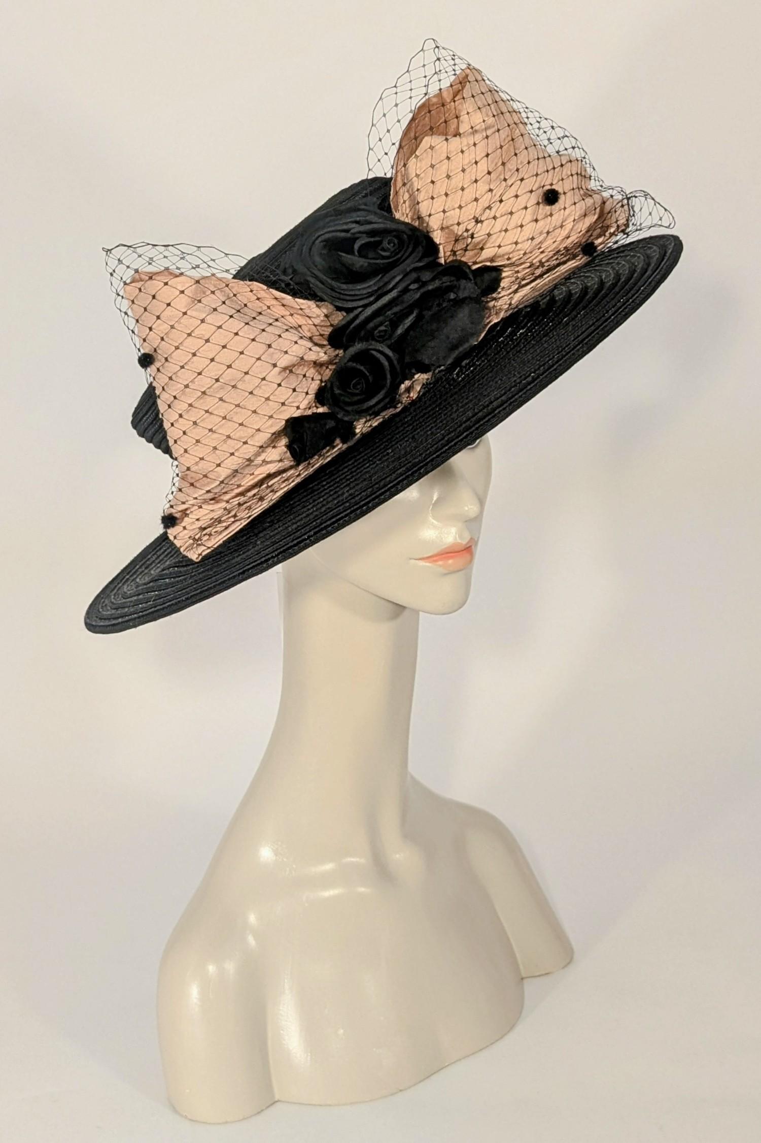 Questo cappello anni '80 a cerchio largo è perfetto per un matrimonio o per una giornata alle corse. È un modello oversize con un favoloso fiocco sul davanti, realizzato in morbida seta rosa polverosa e ricoperto da una rete nera maculata. Questi