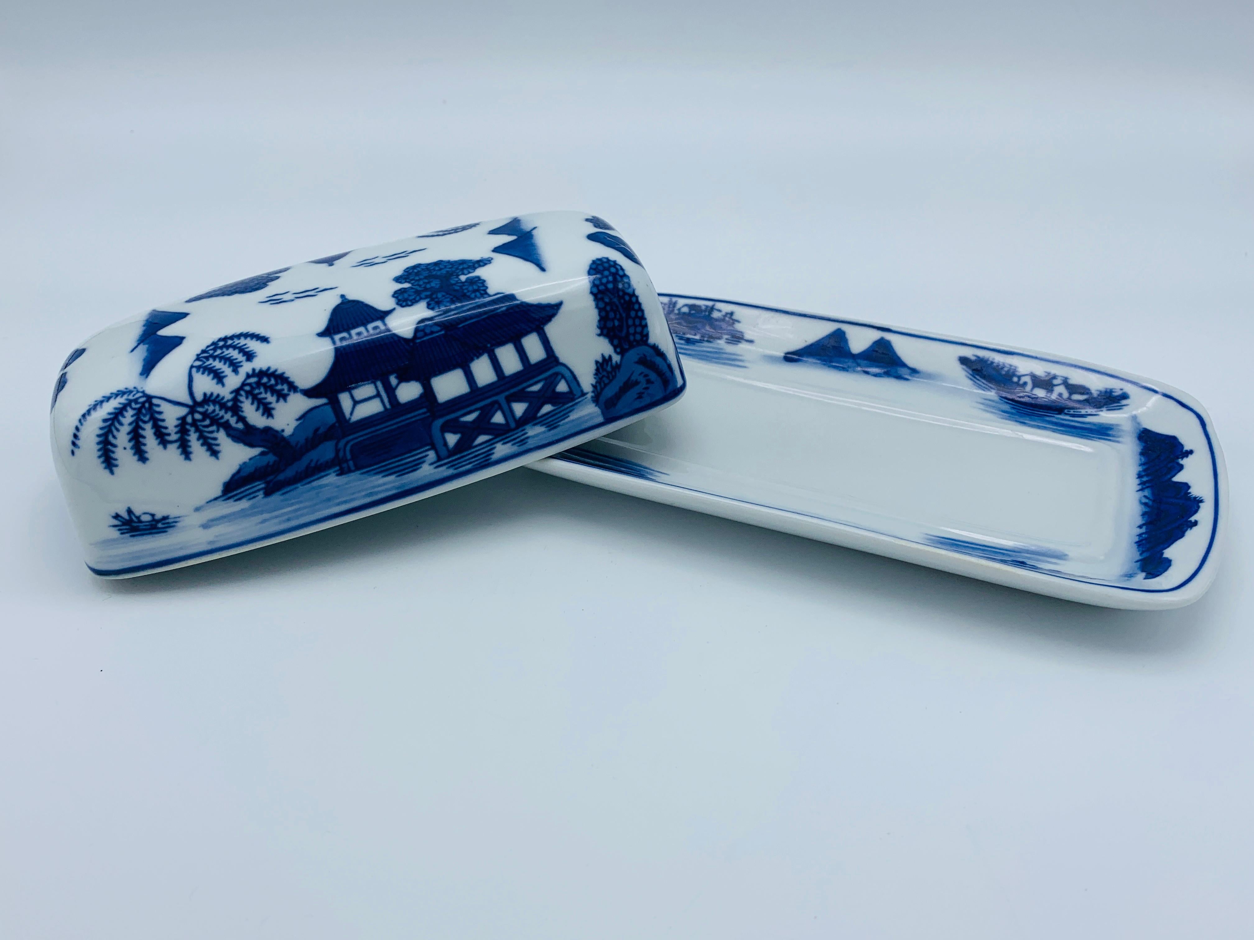 Listed is a 1980s blue and white Chinoiserie porcelain butter dish. The dishes design is in the style of the classic 'Blue Willow' pattern. Heavy, weighing nearly 2lbs.
