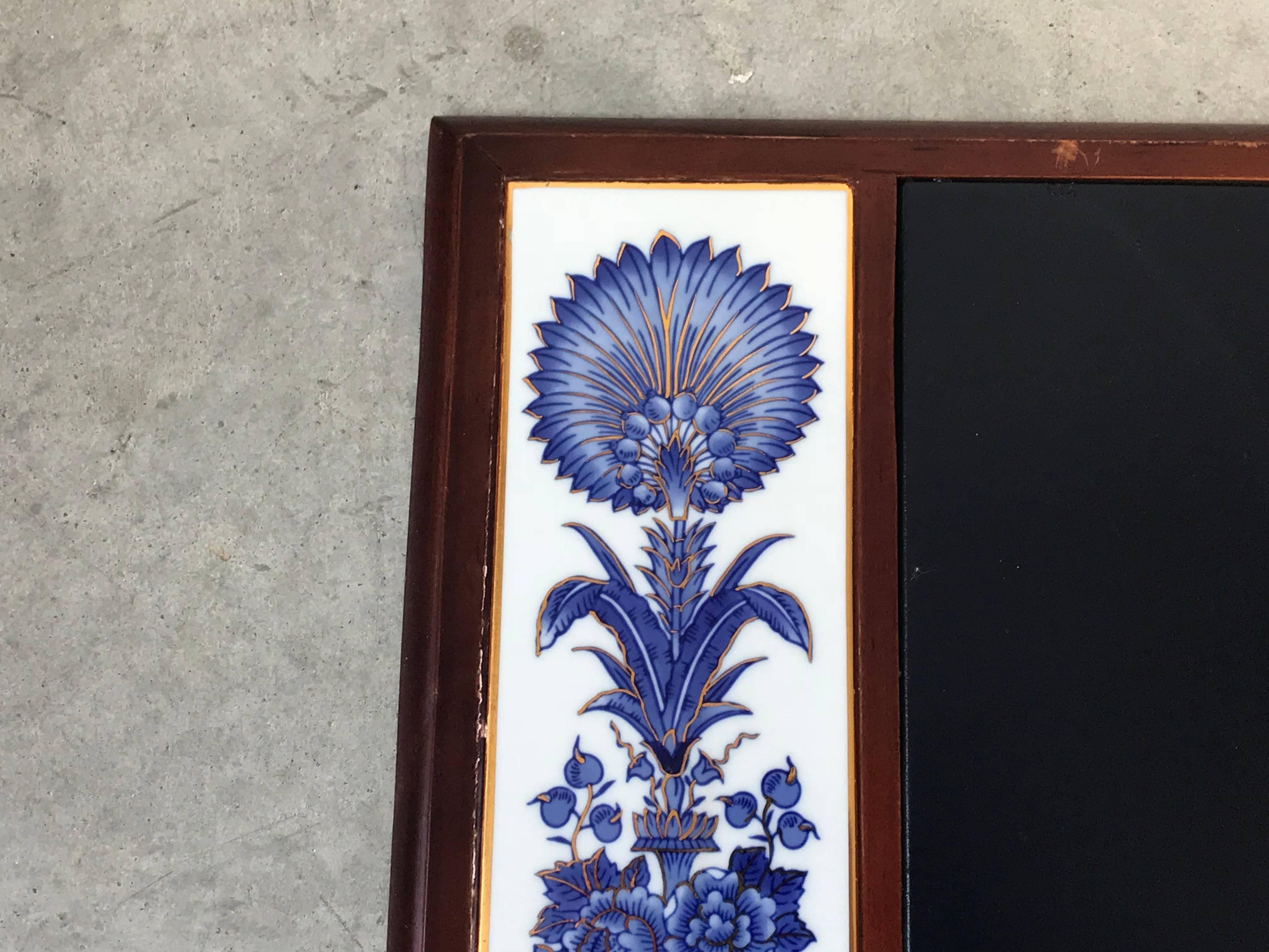 Listed is a beautiful, 1980s blue and white chinoiserie desk pad. The left and right side, have mirrored hand-painted floral motif on porcelain tile inserts. The writing surface is a deep, navy blue leather with a wood border. Heavy. Backside is