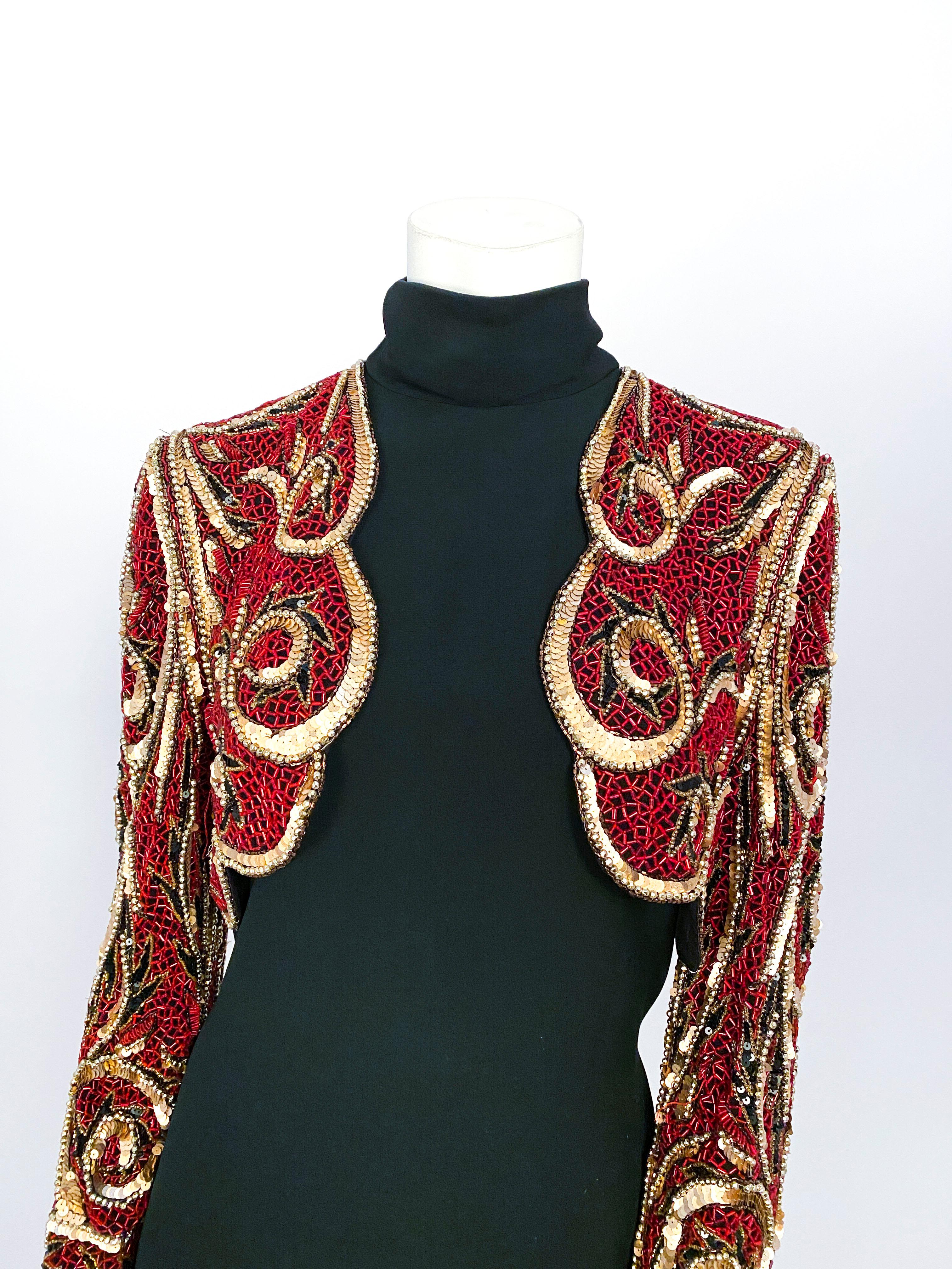 1980s Bob Mackie black rayon crepe high-neck dress with a faux beaded bolero that is attached. The faux bolero is entirely adorned with red glass beads, gold and black sequin. Completely lined and finished with a back zipper closure.