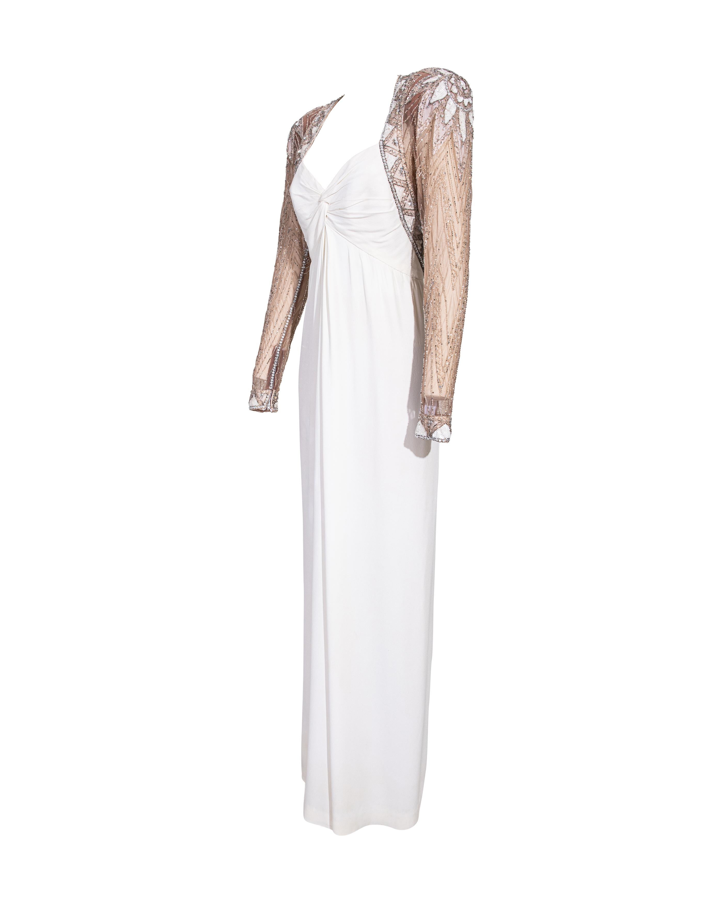1980's Bob Mackie semi-sheer white embellished gown. Upper features heavily embellished tan mesh, while lower is white silk skirt with slight drape throughout. Semi-sheer mesh creates appearance of open back. Concealed center back zip closure with