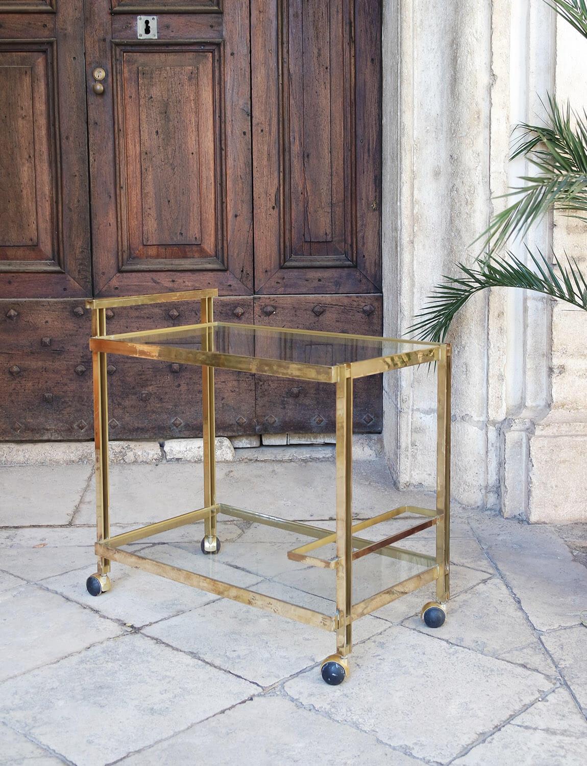 An Italian brass drinks trolley likely made in the 1980s. It has a brass frame and two glass shelves as well as an area on the bottom shelf to store three wine bottles. The trolley has four rubber wheels. This is a beautiful piece. Please note as