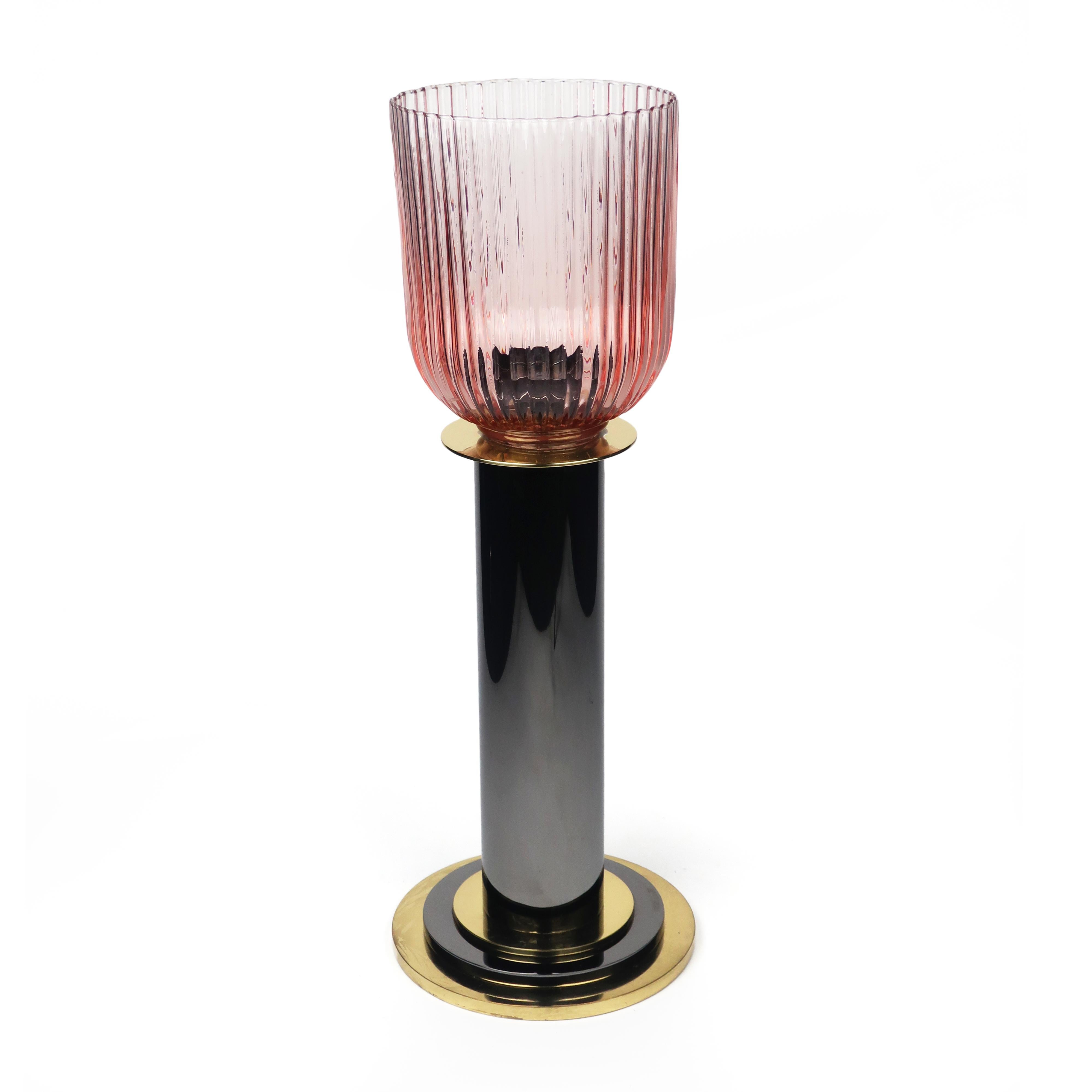 A large candleholder with a brass and dark grey metal base and a pink glass hurricane shade. Purchased from Lorin Marsh in the 1980s, this piece shows both a Memphis Milano and Art Deco design influence.

In excellent condition with wear