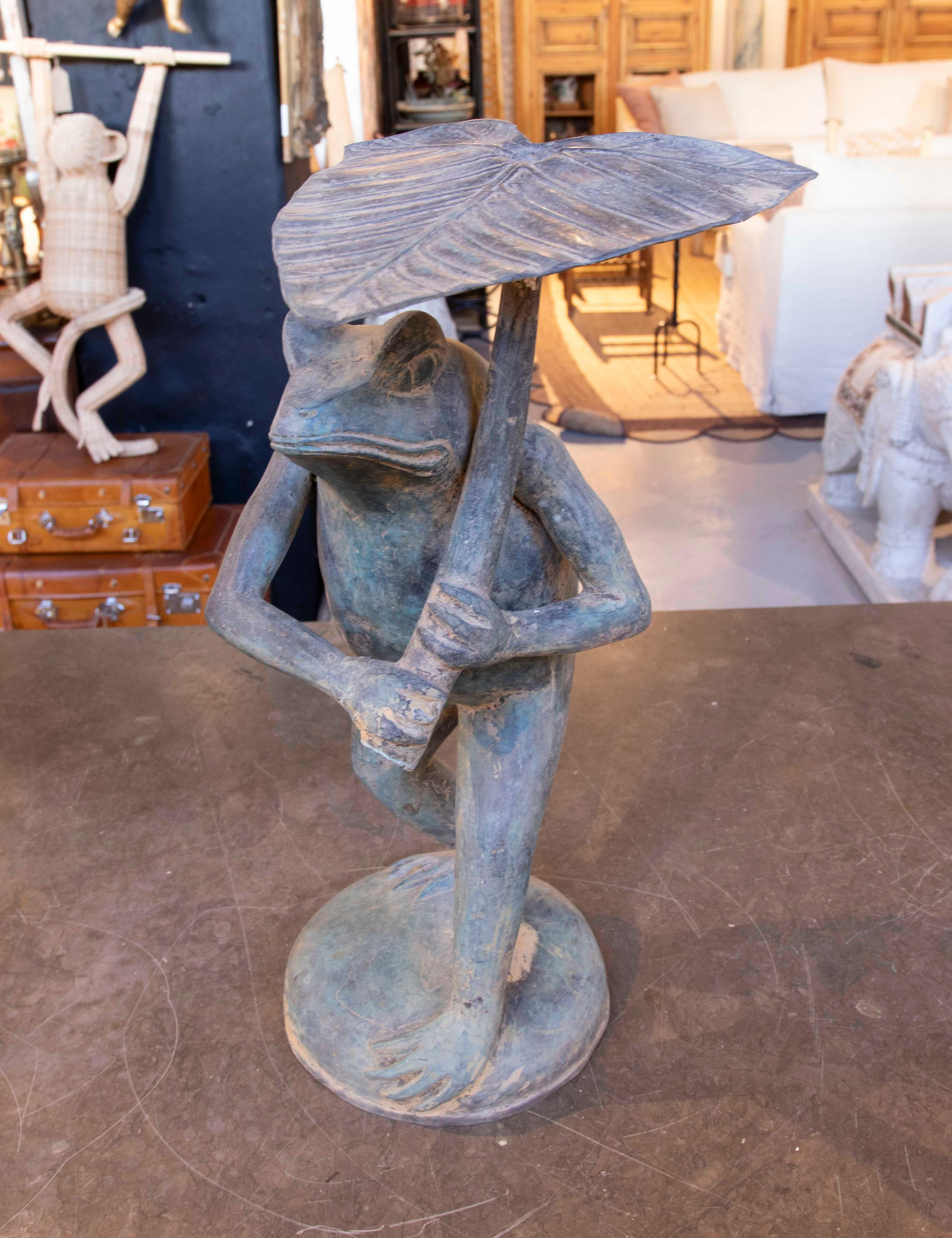 Funny and original frog sculpture made of bronze, with a design that shows it holding a parasol with leaf-shaped details. Its aged finish gives it a rustic and charming touch, ideal for decorating gardens, patios or themed interiors. This piece