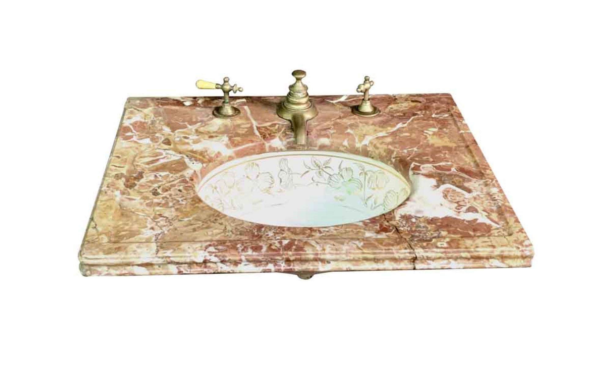 1980s bathroom vanity top with a single basin. The marble vanity top consists of tones of deep brown, amber, white, and red veining, and the white sink has a gold floral design around it. The original handle and faucet hardware are included. One