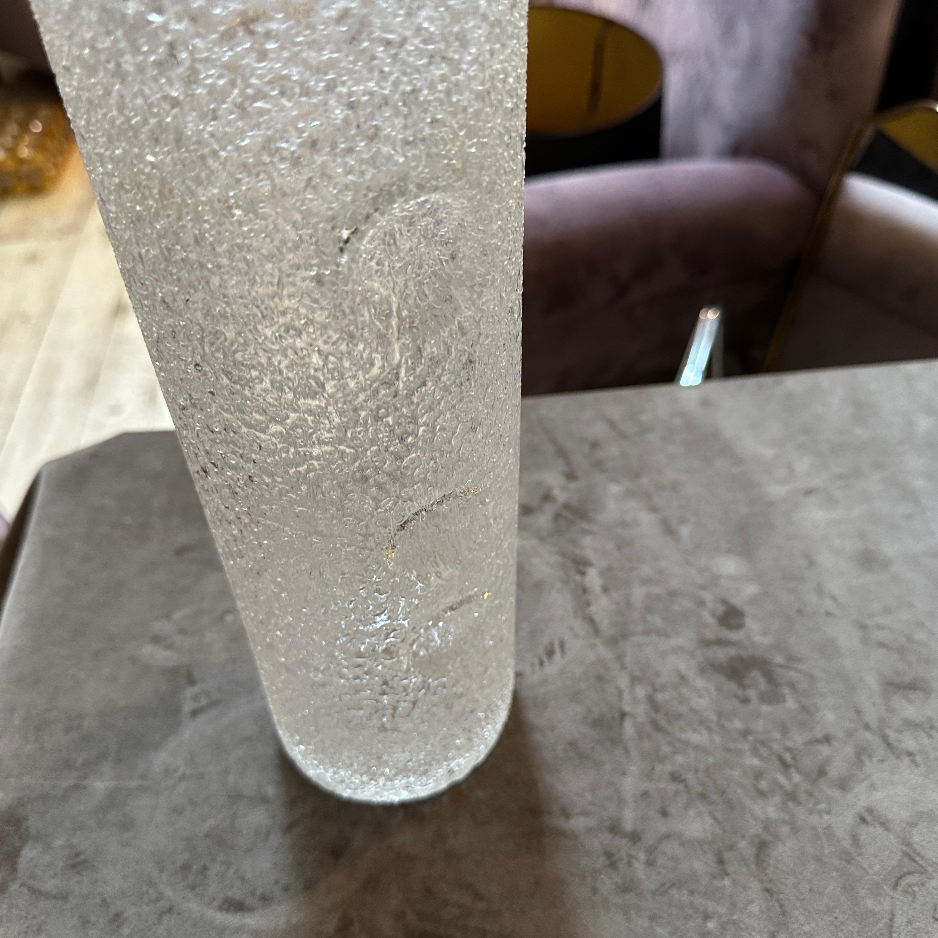 Se trata de un jarrón cilíndrico de cristal transparente, caracterizado por una superficie 