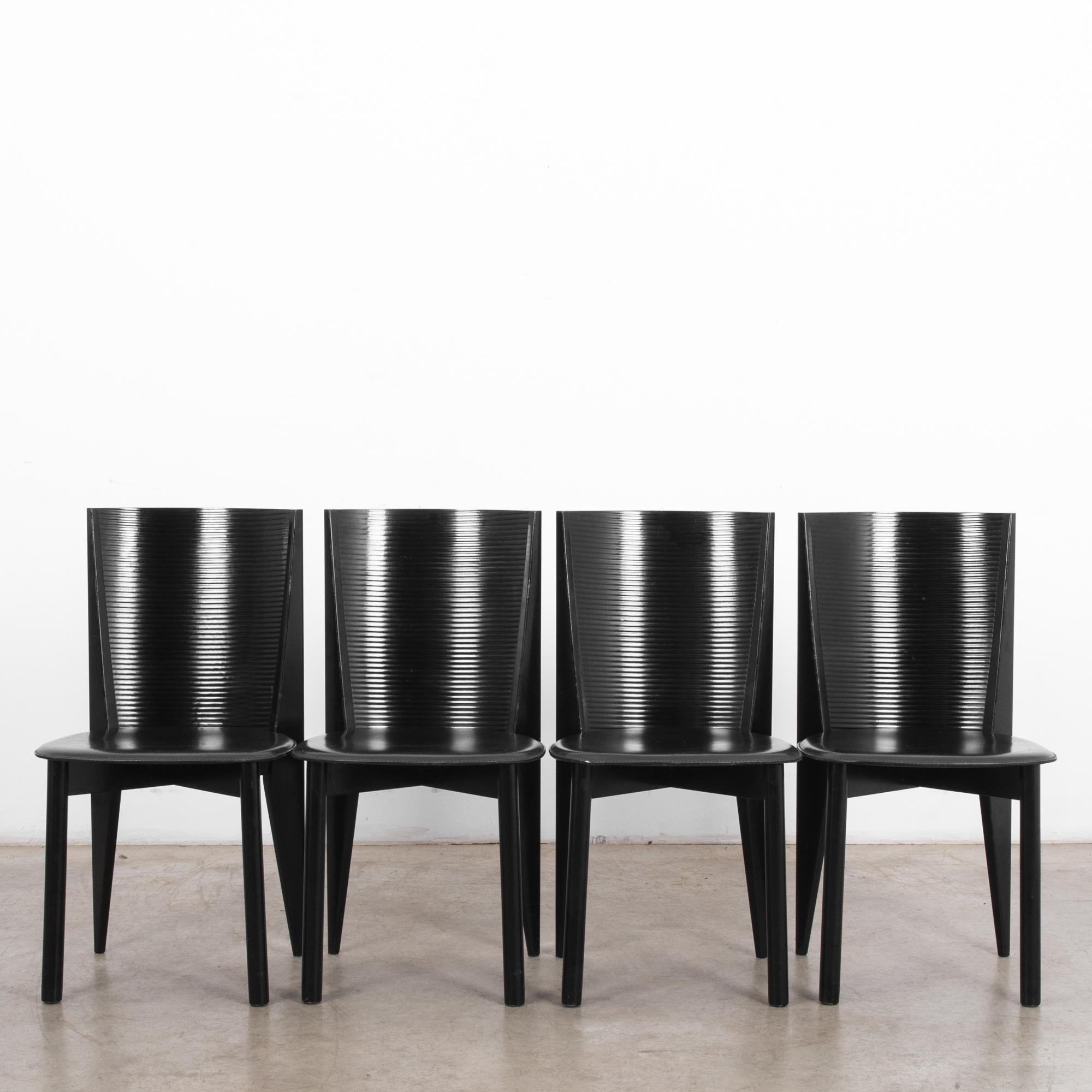 This set of four black wooden chairs by Calligaris was made in Italy, circa 1980. These dining chairs feature a curved back with ridges and leather seats. The tapered and angular rear posts counterbalance the cylindrical front legs of this stylish