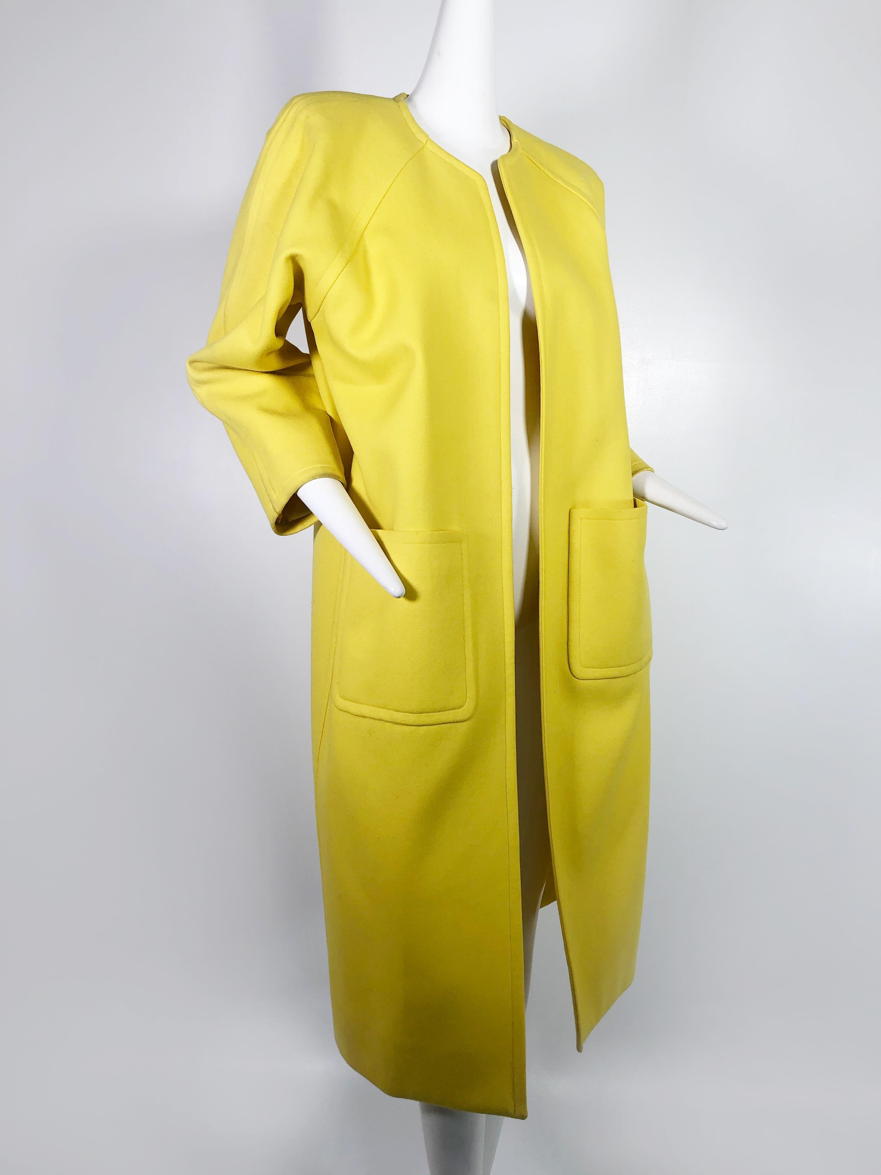 1980s Canary yellow wool overcoat with deep hip pockets and raglan sleeves with shoulder pads. Welted seams throughout. No closures. 