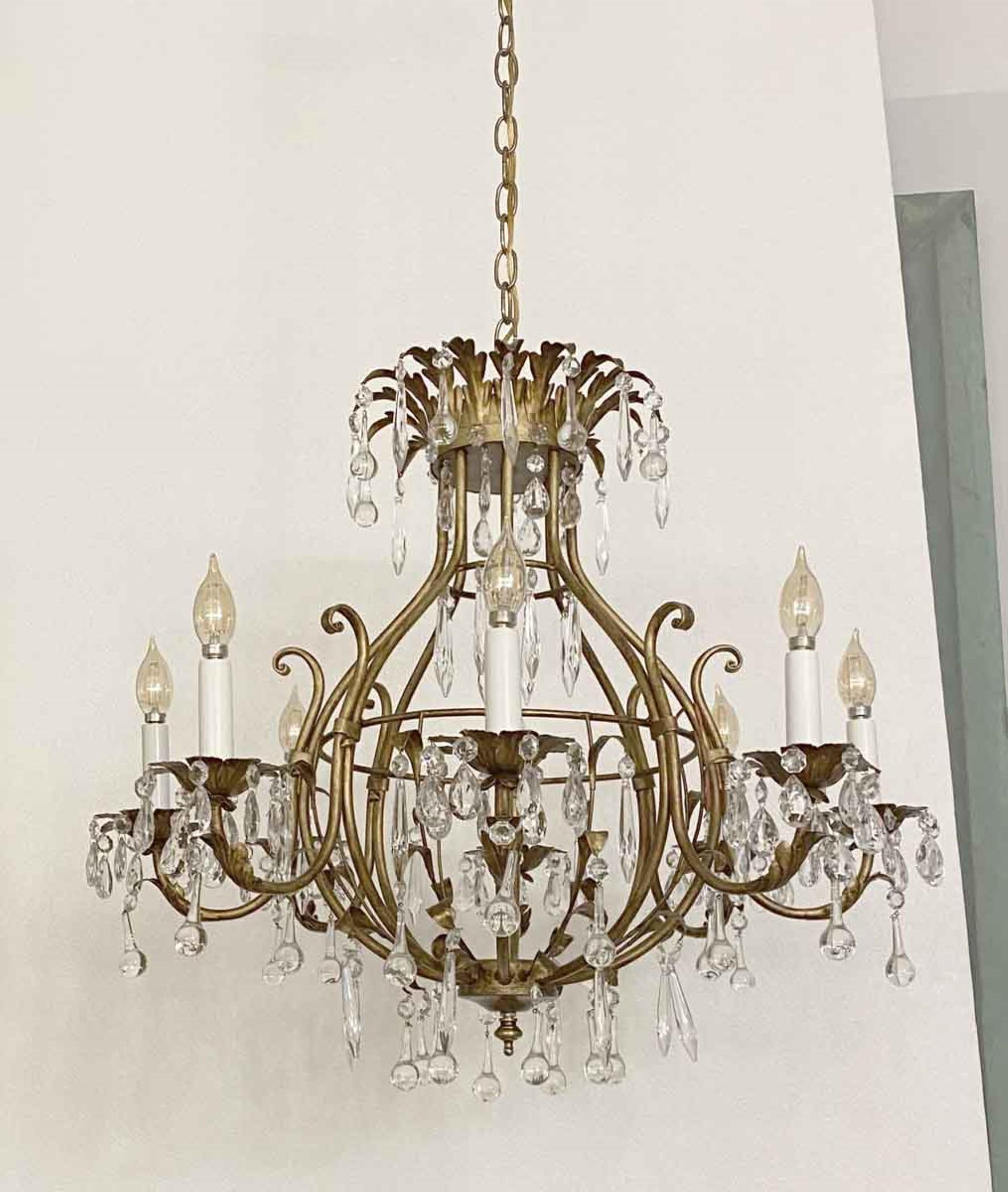 This 1980s chandelier has flower bobeches along with a leaf design crown, in the Florentine style. It displays teardrop crystals and gilt metal, with a round globe-like center. There are eight lights which take candelabra bulbs, up to 60W max.