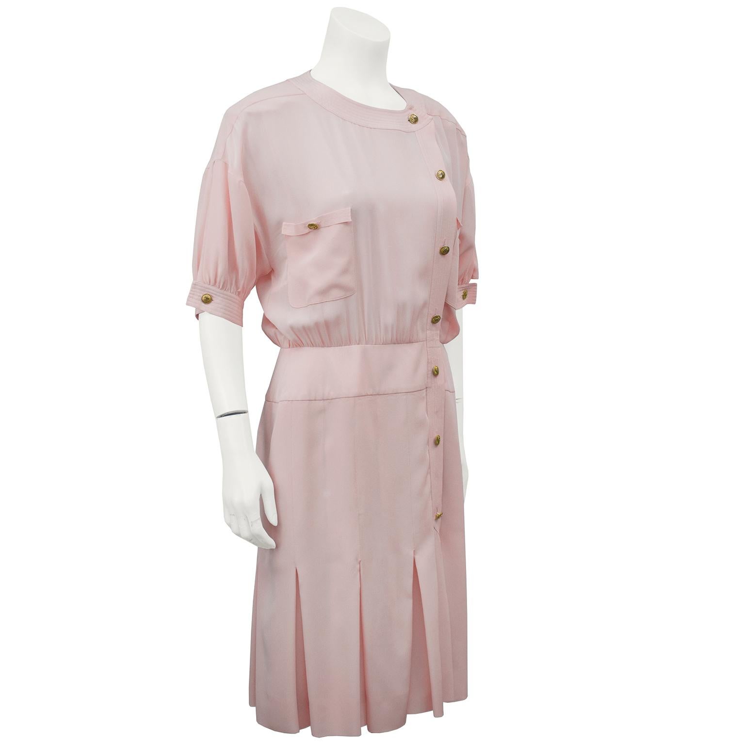 Classic style Chanel day dress from the 1980's. The off center button placket is complimented with two front patch pockets. The sleeves fall to the elbow and the cuffs are finished with goldtone Chanel buttons. Cinching at the natural waist, the