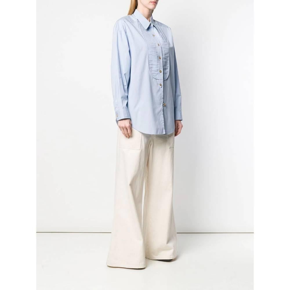 Chanel shirt in light blue and white checked cotton, with classic collar, front closure with golden logoed buttons and decorative pleats, long sleeves and cuffs with button. Rose-shaped brooch on the chest.
Years: 80s

Made in France

Size: 44