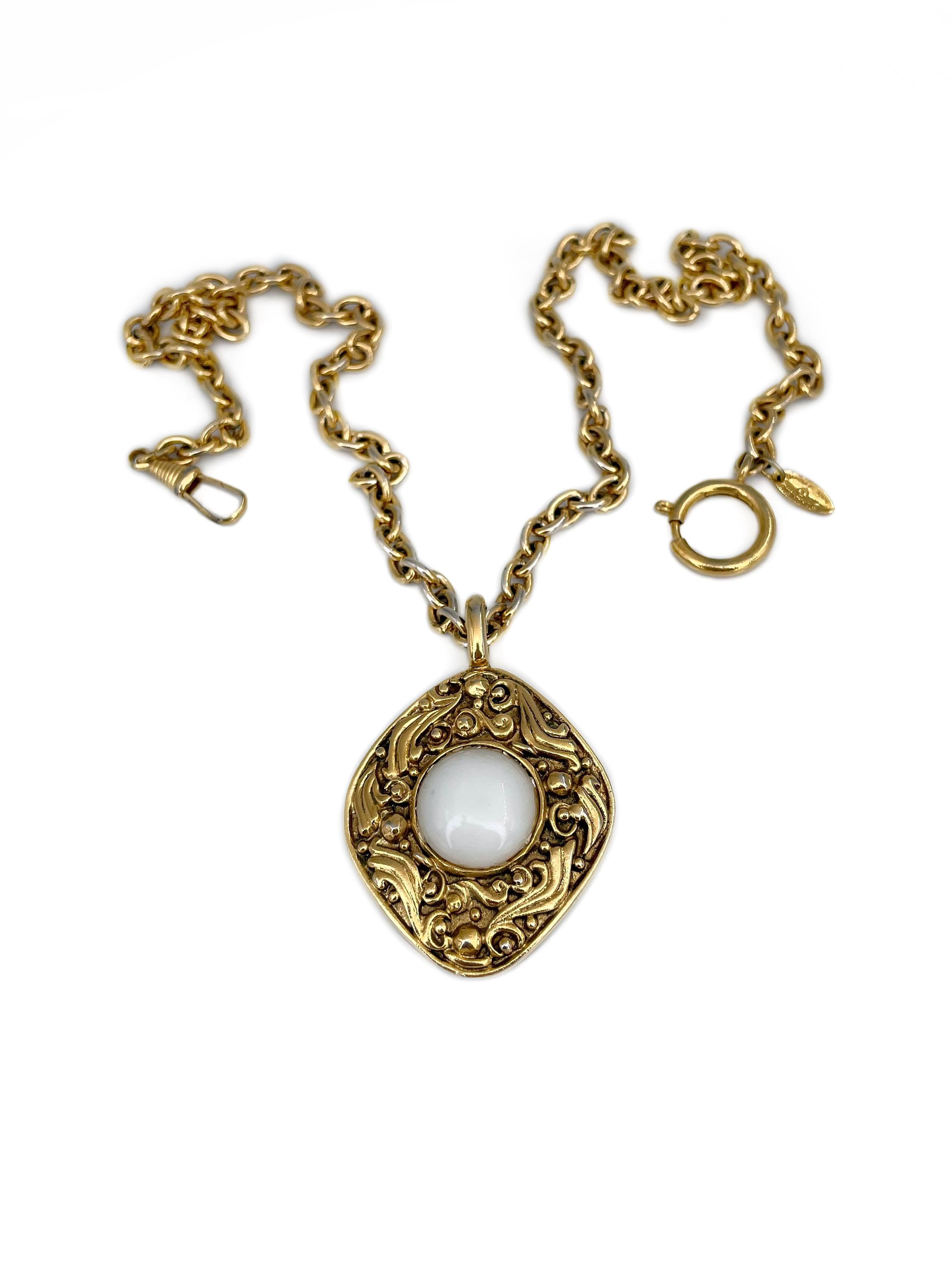 Il s'agit d'un pendentif en forme de losange avec une chaîne conçu par Chanel dans les années 1980. La pièce est plaquée or. Il est orné d'une résine blanche au centre. 

Signé : 