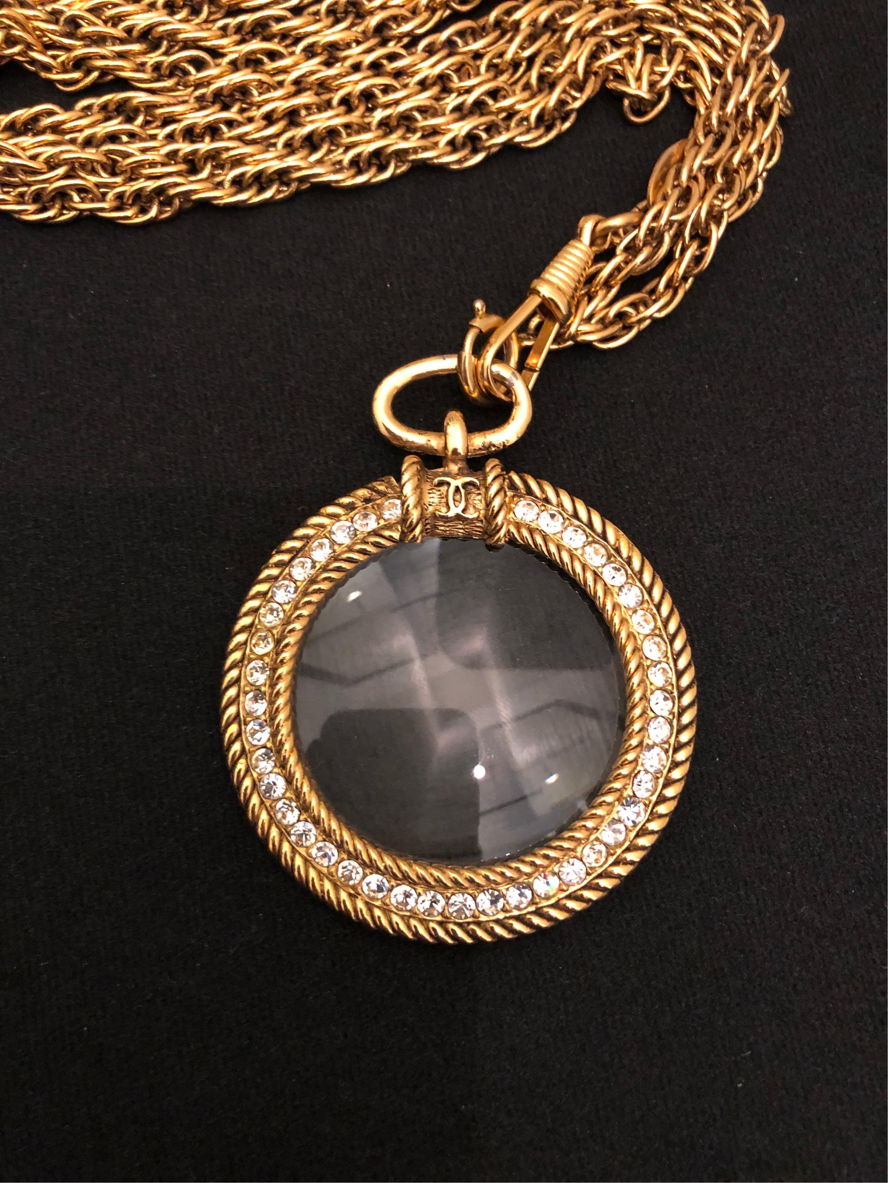1980s Chanel double gold toned chain necklace featuring a rhinestone encrusted magnifying lens. Spring ring fastening. Stamped Chanel 1984, made in France. Total length 90 cm (35.5 inches) Magnifying lens 5 cm in diameter. Comes with box.