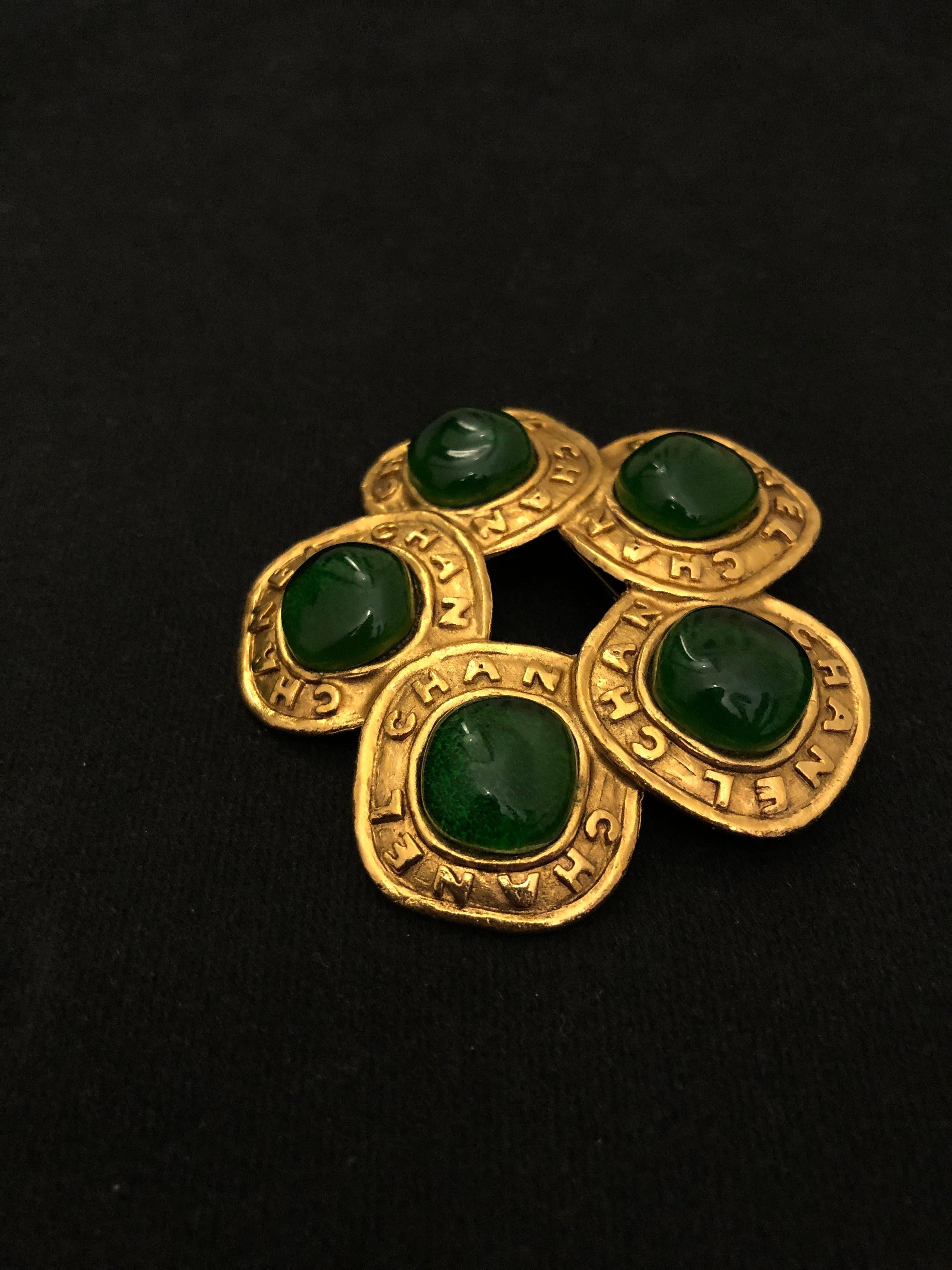 1980s Chanel gold toned brooch featuring five green colored gripoix surrounded by gold toned CHANEL letter frames. Stamped CHANEL 2 6 made in France. Measures approximately 6.2 x 6 cm. Comes with box. 

Condition: Minor signs of wear. Generally in