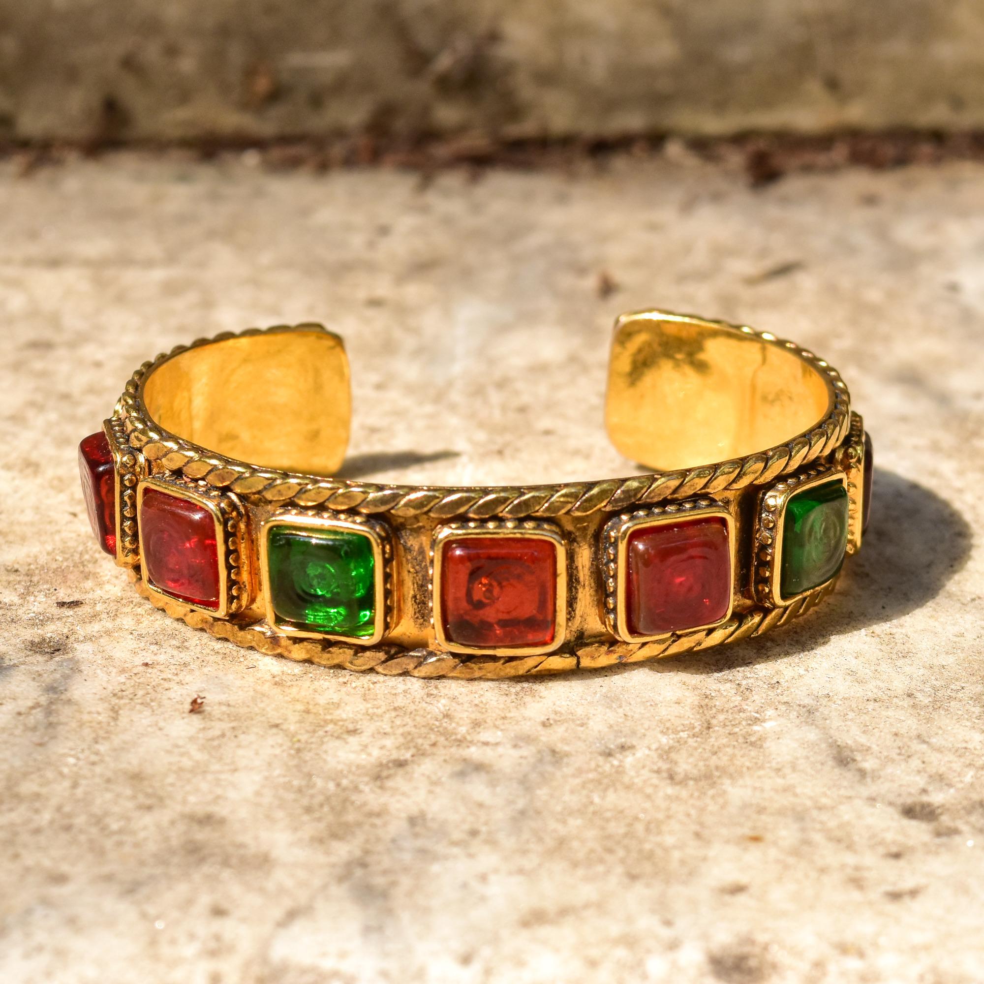 Setzen Sie ein Zeichen mit diesem Manschettenarmband aus Glas im Vintage-Stil von CHANEL gripoix. Mit einer 3/4 Zoll breiten goldfarbenen Manschette mit geflochtenen Verzierungen und mehrfarbigen Glasverzierungen. Die gegossenen Glasmotive in