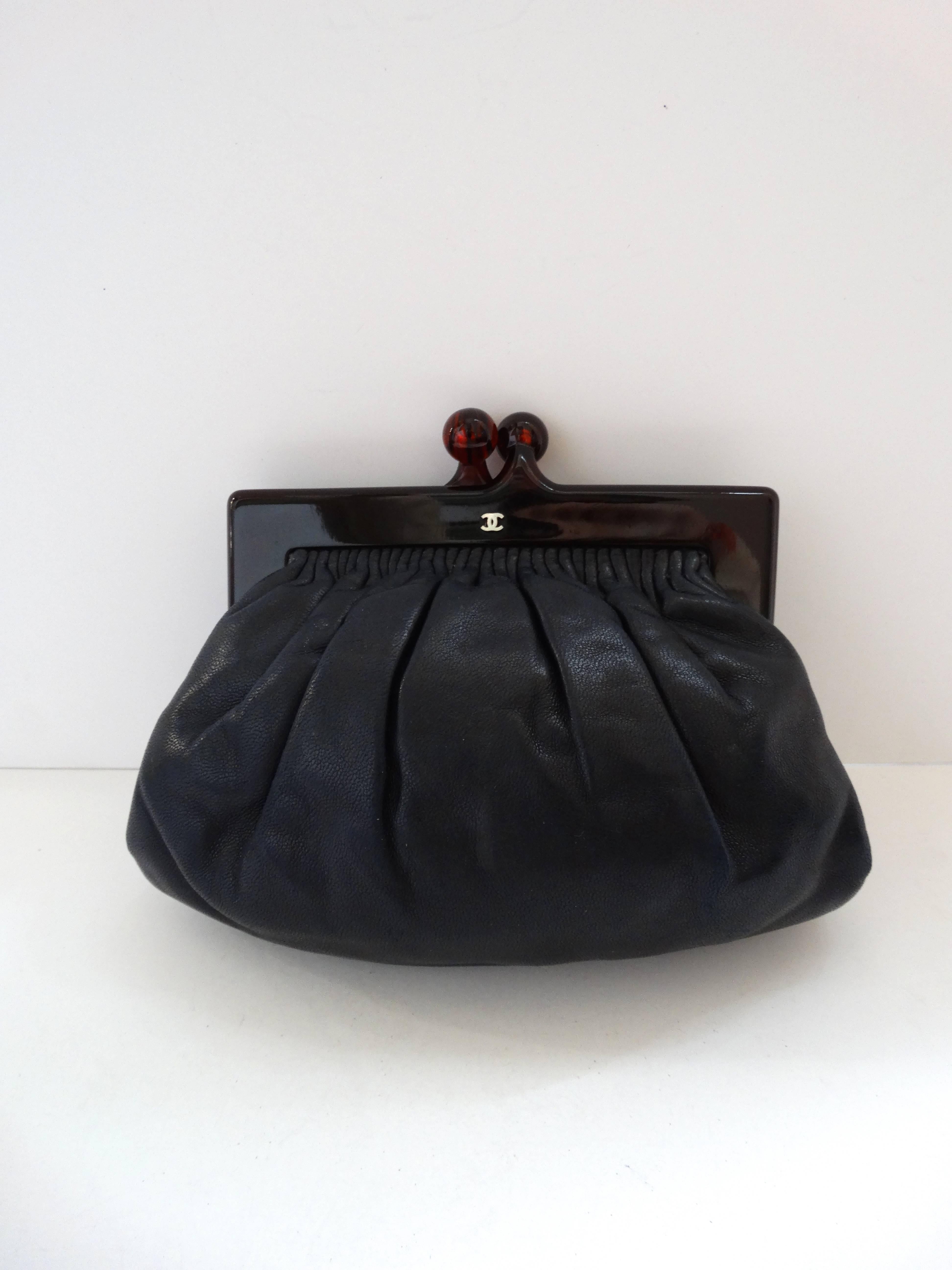 The most adorable little pouch bag from iconic handbag house- Chanel! Made of a soft lambskin leather in a deep, dark navy color. Marbled lucite frame construction with kiss-lock closure at the top. Small silver toned metal CC below the kiss-lock.