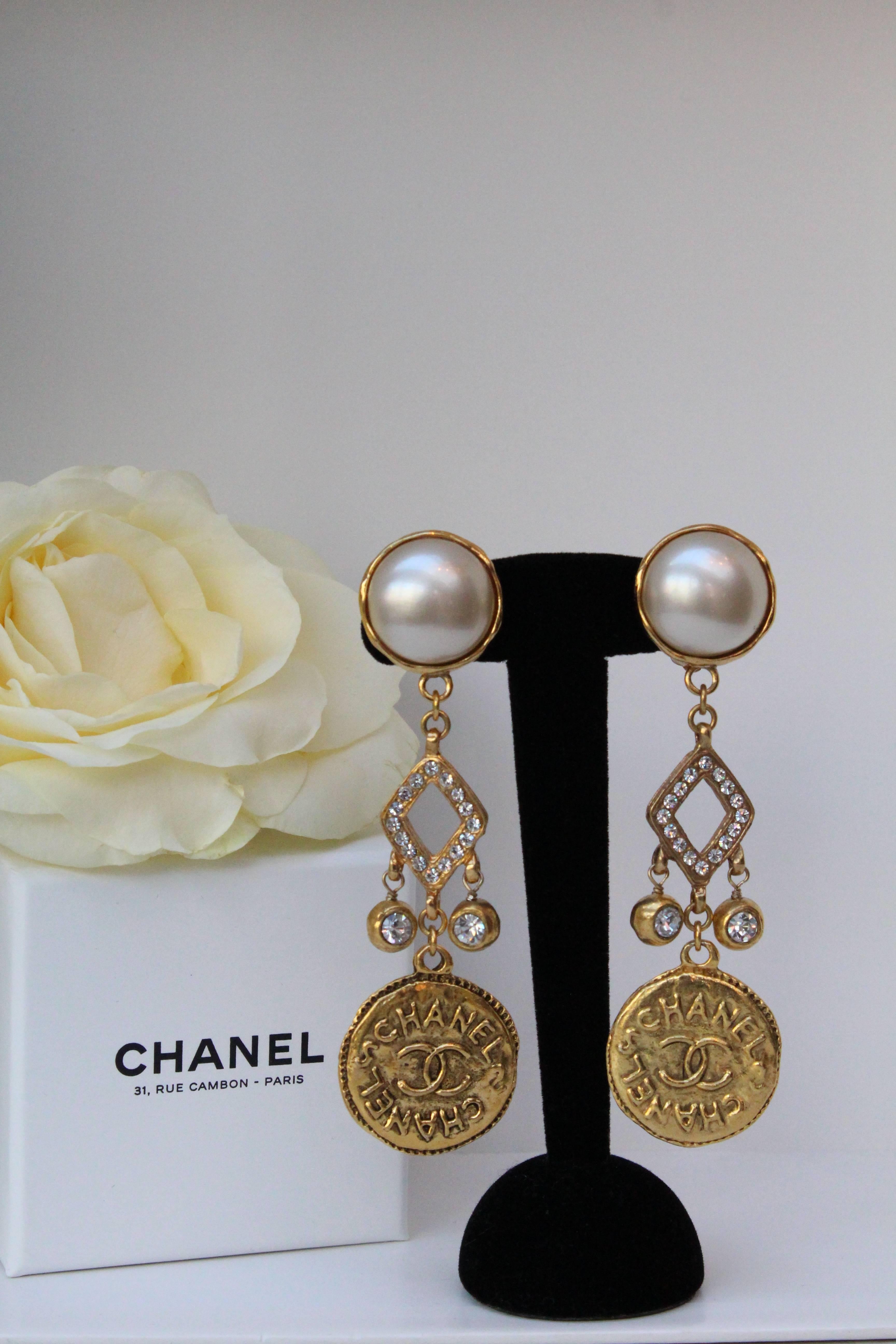 CHANEL (Made in France) Beautiful pair of drop clip-on earrings, comprised of a pearly cabochon and an openwork diamond-shaped gilded metal setting paved with rhinestones and holding two articulated rhinestones. The bottom part is decorated with a
