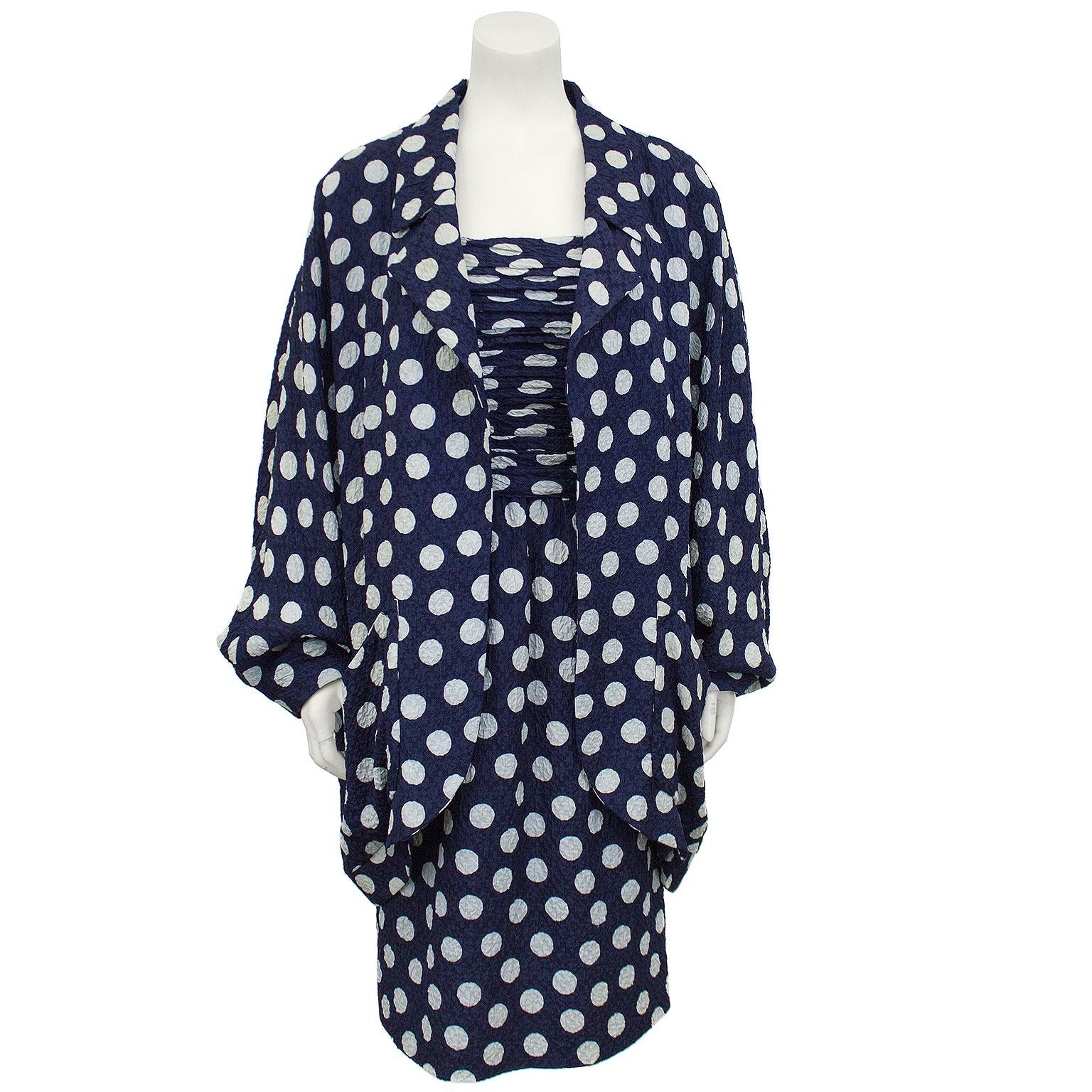 Beautiful 1980s Chanel silk navy polka dotted strapless dress and jacket. The busts of the dress is pleated to the natural waist and the skirt falls to mid calf length. Zipper up the back. The voluminous jacket has a shirt lapel and poet style