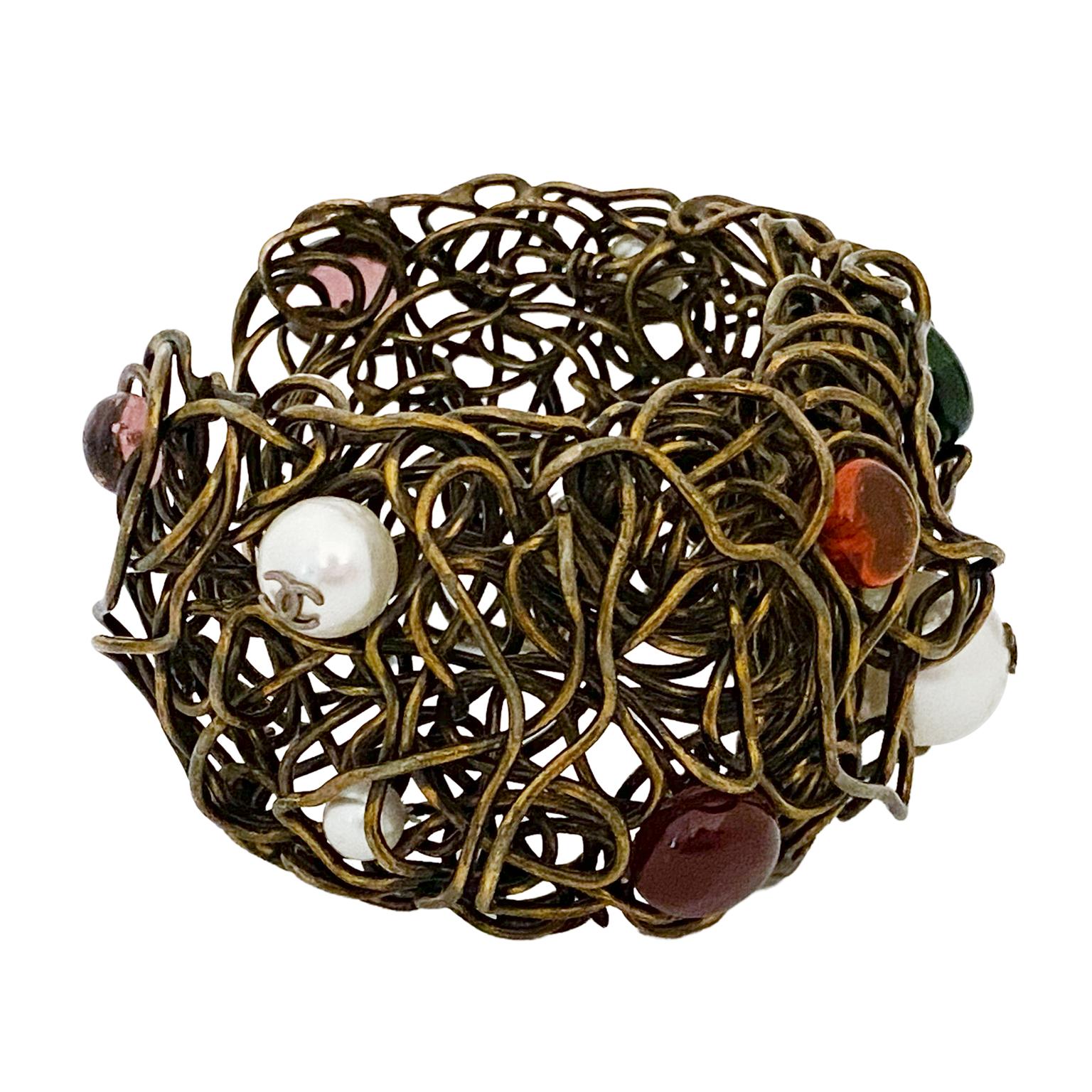 Interesting and unique 1980s birds nest style Chanel cuff. Brass tone metal wire abstractly designed and molded into a cuff. Embellished with dark red, dark green, purple and yellow poured glass cabochons. Three pearls with Chanel CC logos.