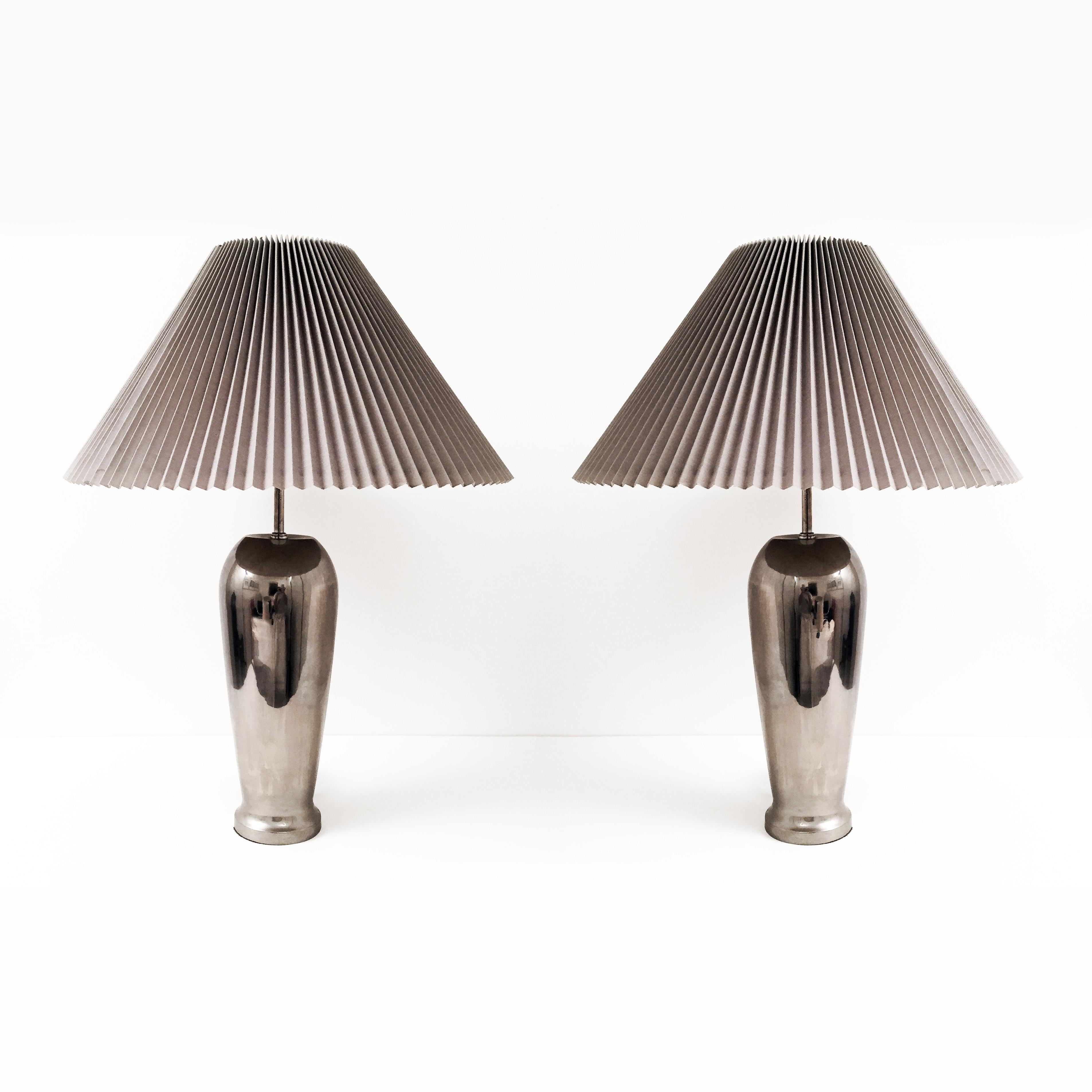 A unique pair of chrome table lamps in the shape of elongated urns and tall neck fitting for the lamp with the original knife pleat hardback shades. Very modern and elegant design brought from the 1980s glamour.