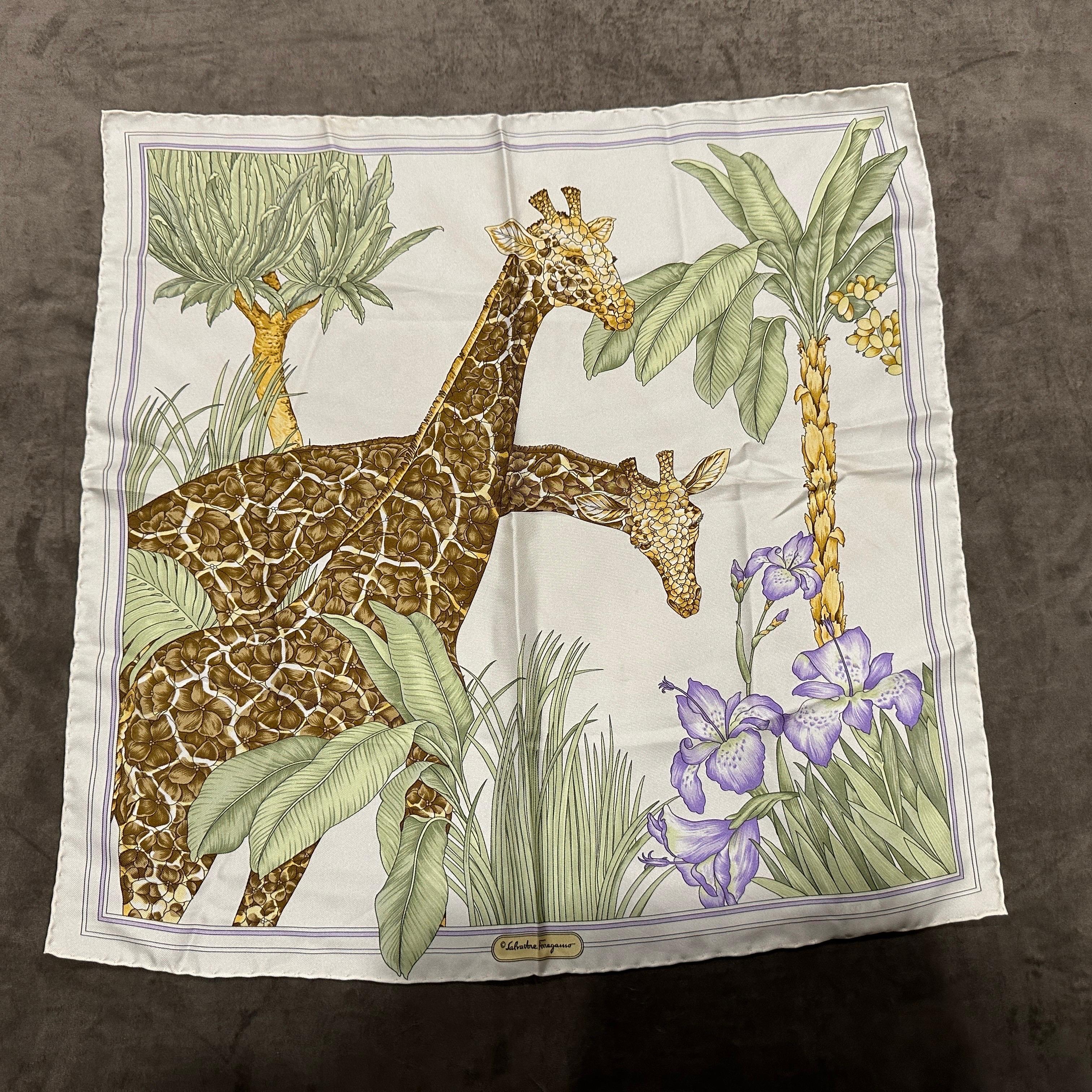 Questo raffinato foulard in seta anni '80 di Vincenzo Ferragamo unisce l'arte ispirata alla natura a un'eleganza senza tempo. Il disegno presenta due graziose giraffe in mezzo a un paesaggio tropicale lussureggiante di iris vivaci, palme imponenti e