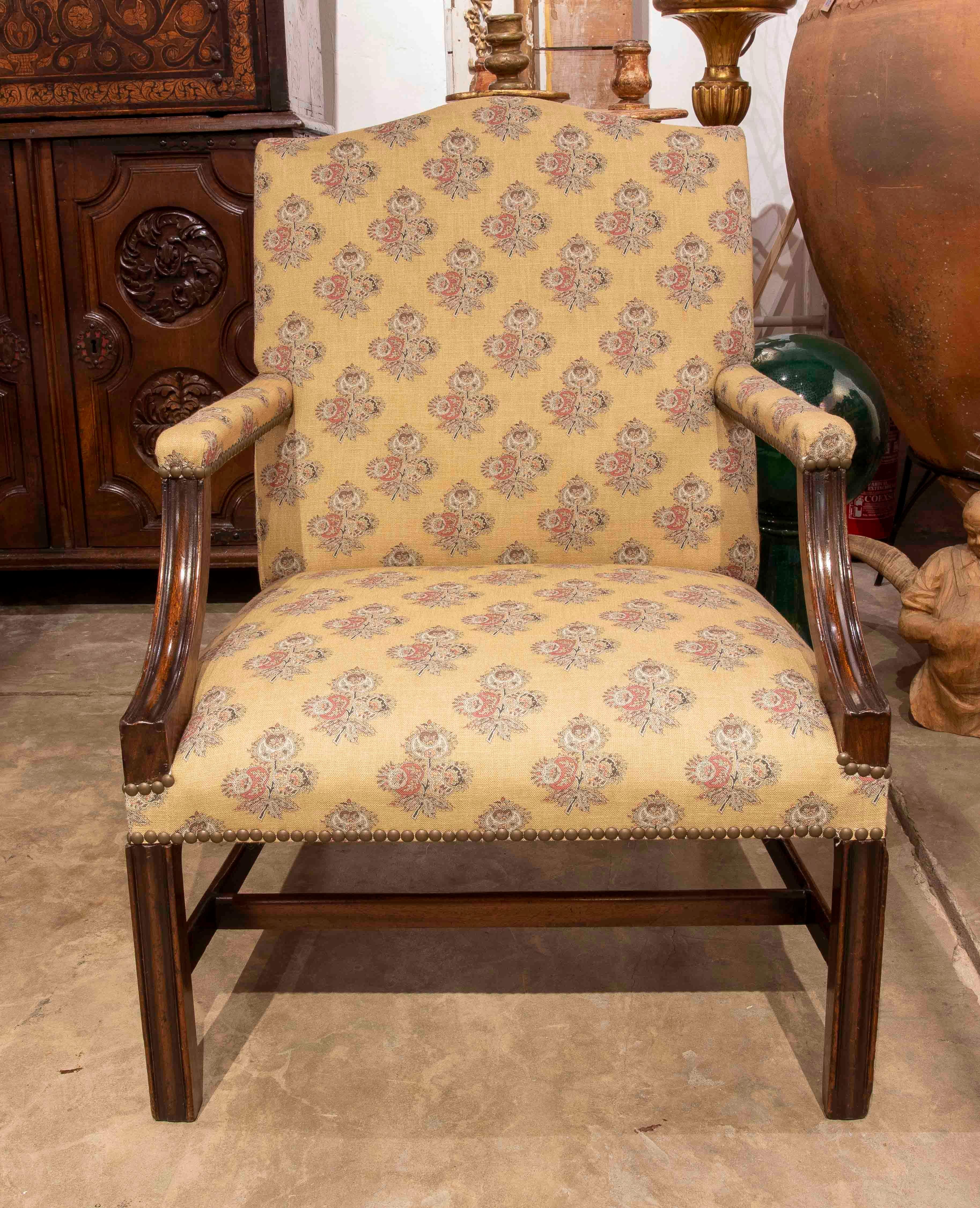 Traditional-style armchair with a dark-finished solid wood frame and elegant mustard fabric upholstery with a floral motif repeated in soft tones. The straight backrest and crossed legs provide stability and a restrained silhouette that fits into