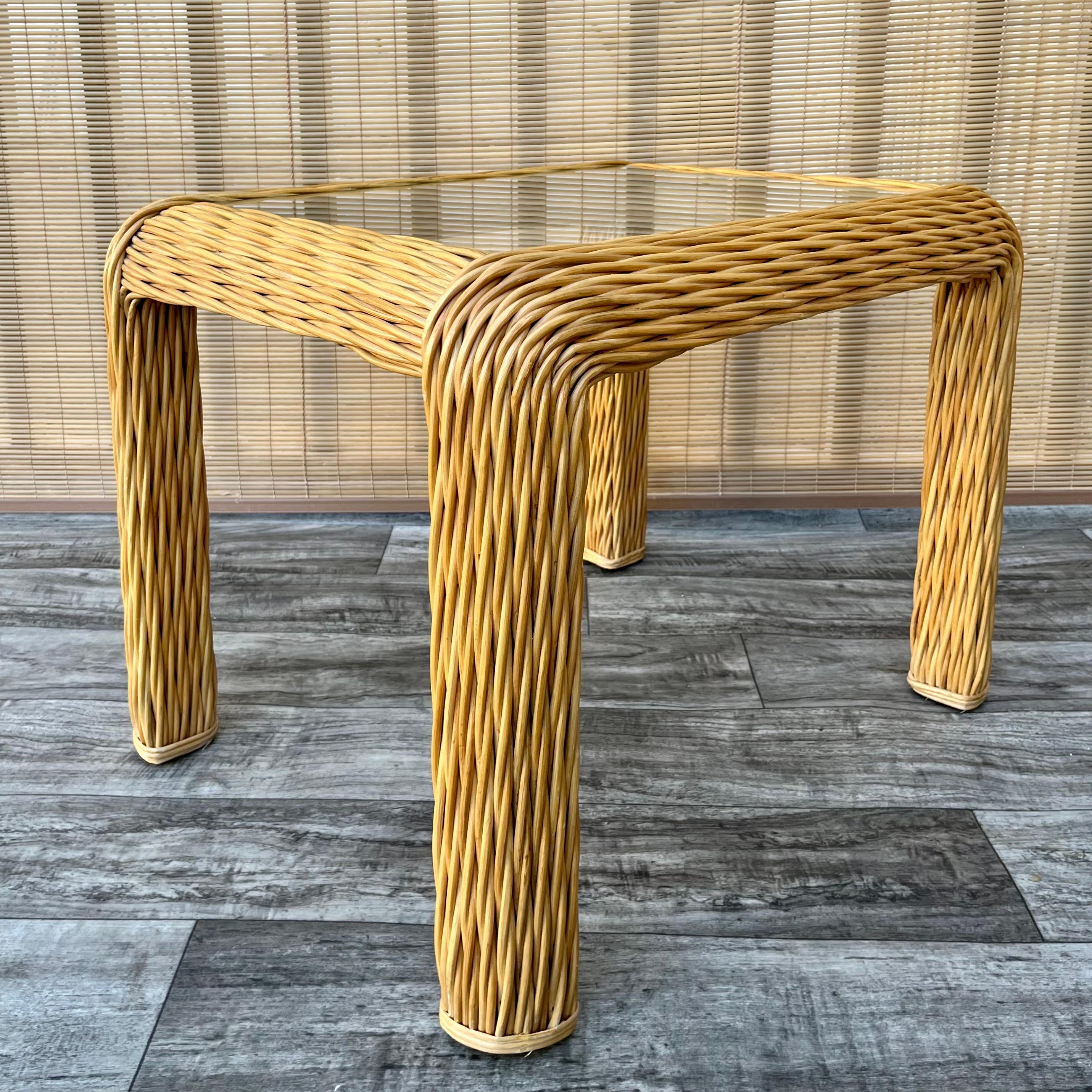 Vintage Coastal Style Braided Pencil Reed Rattan Side Table in the McGuire Style. circa 1980s.
Features sophisticated curves, an elaborated braided pencil reed construction and an a glass top.
In excellent original condition with very minor sings
