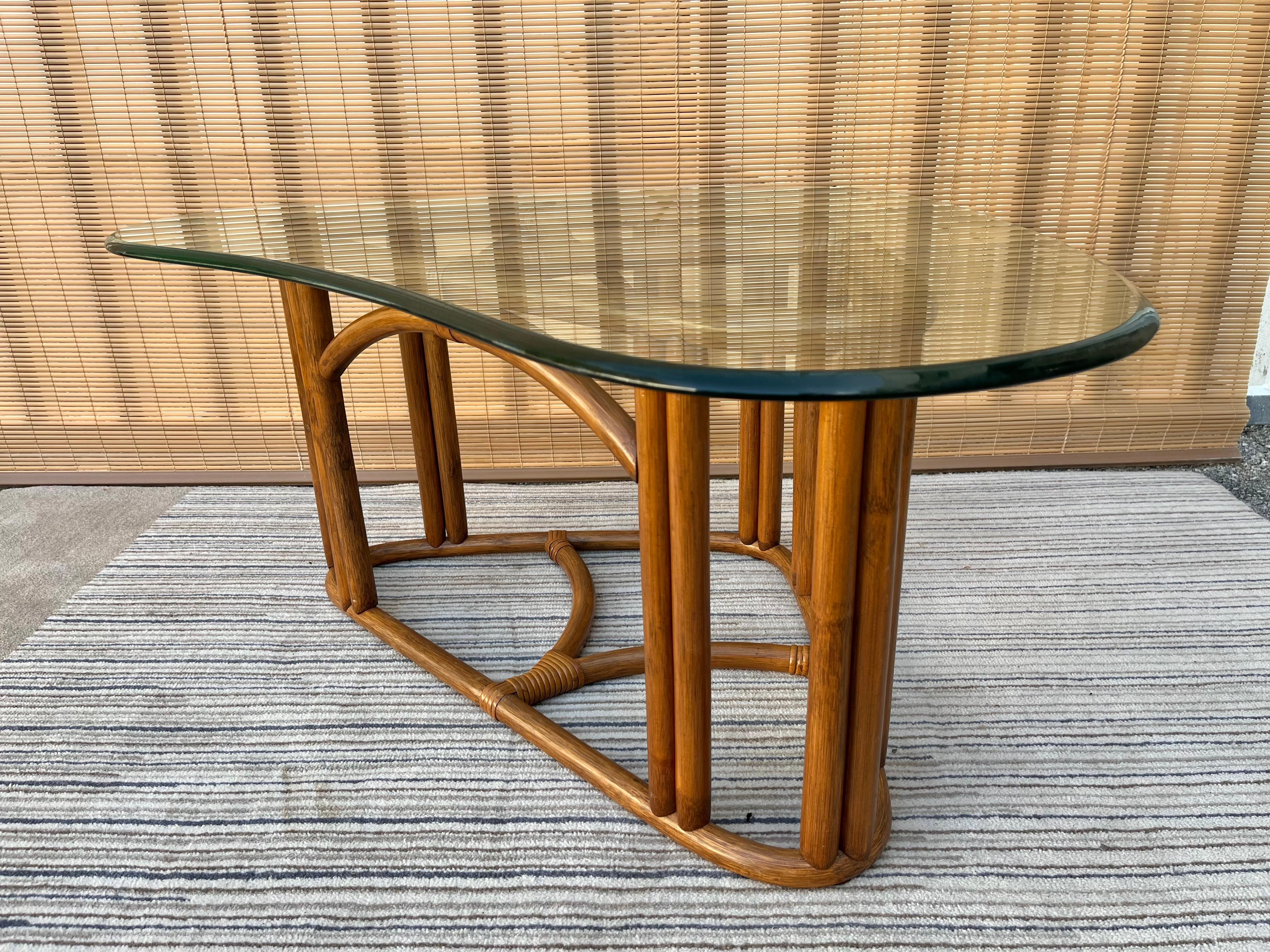 Vintage Mid-Century Modern / coastal style triangular rattan coffee table in the Franco Albini's Style. Circa 1980s.
Features a triangle-shaped rattan and wicker sculptural base with a removable beveled kidney shaped glass top.
In excellent near
