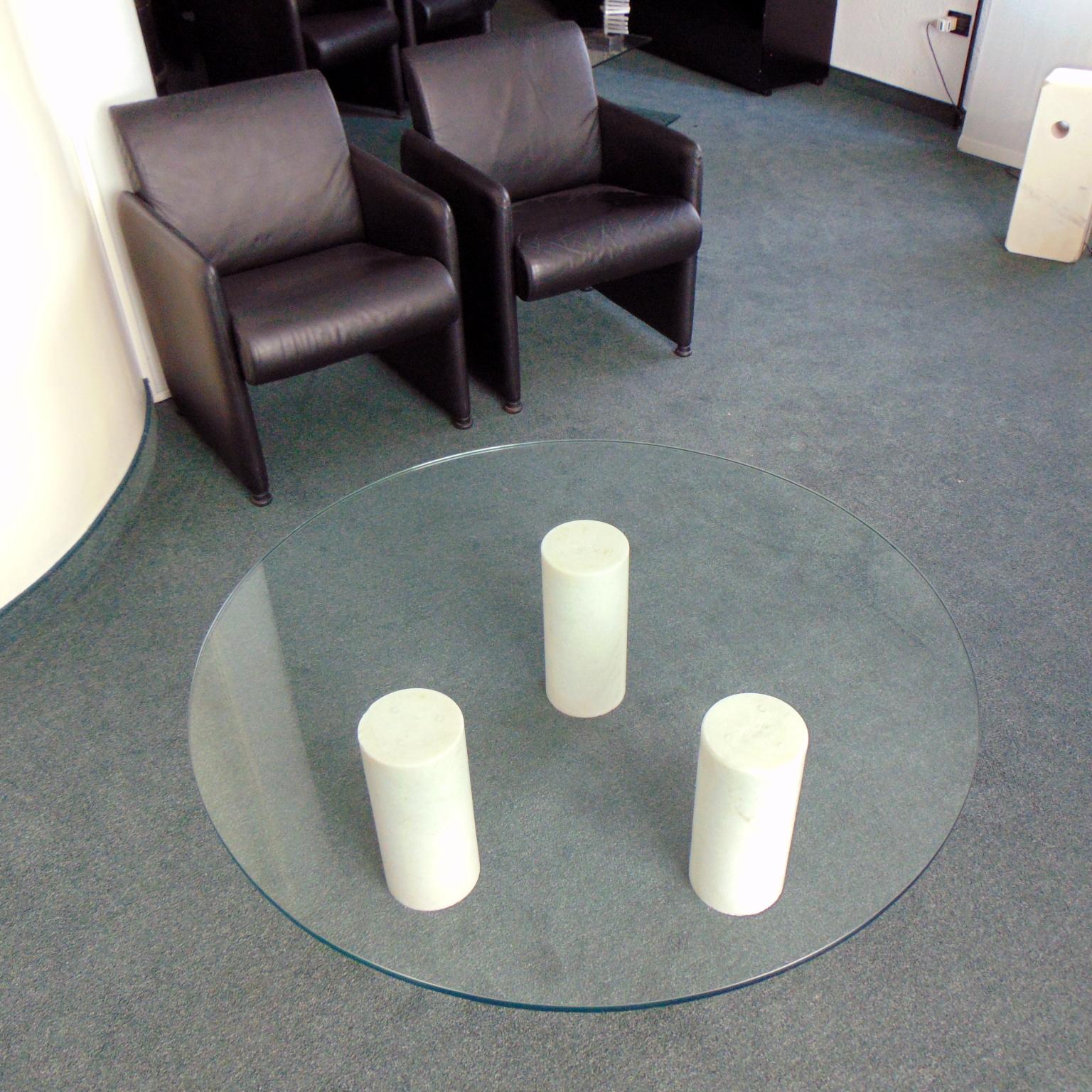 This round, low table has three sculptural cylindric legs in a rare white marble originating from Brescia, Italy. It is a very white marble with crystal inclusions. The legs are polished and very slightly rounded up in the upper part. The glass top