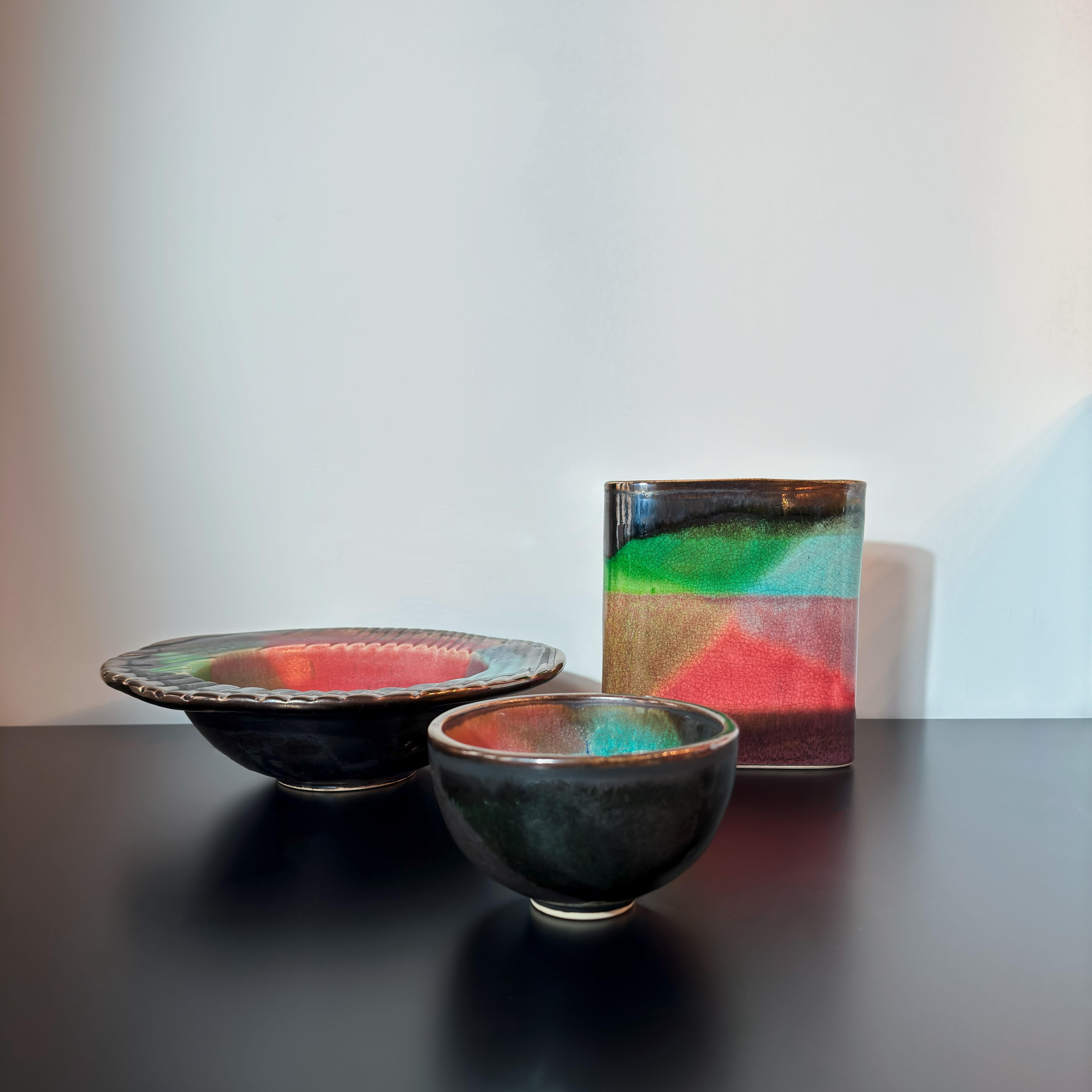 A set of three raku-fired studio pottery pieces, handcrafted in the UK circa 1980s—a visually striking collection of colourful pottery blending modernism with ancient Japanese firing techniques.

The set includes a small bowl (possibly for sake), a