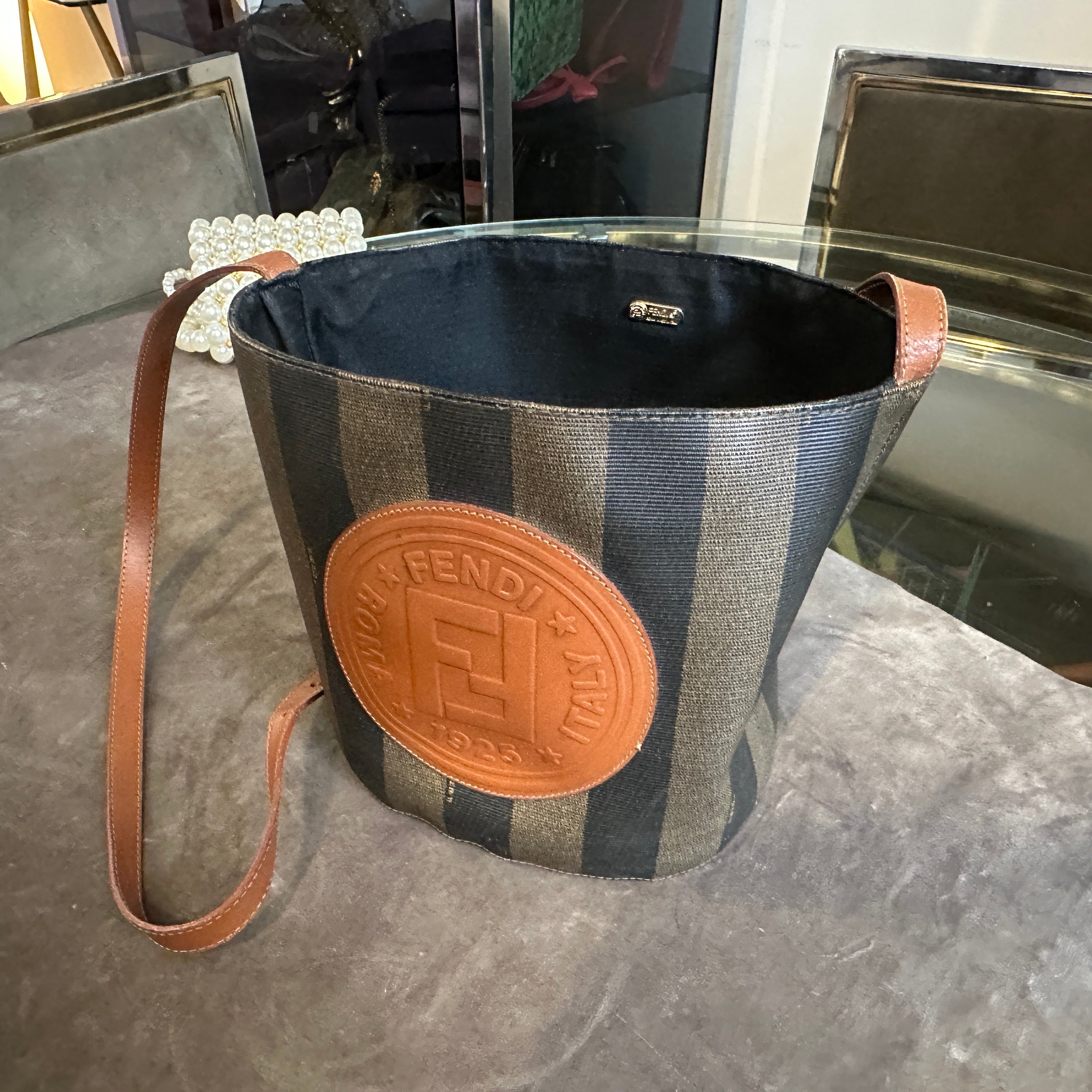 Questa autentica borsa a secchiello Fendi degli anni '80 è un esempio lampante dell'eredità duratura della casa di moda italiana. La borsa presenta l'iconico motivo a strisce Pequin in tela spalmata nera e tabacco, che offre resistenza e una texture