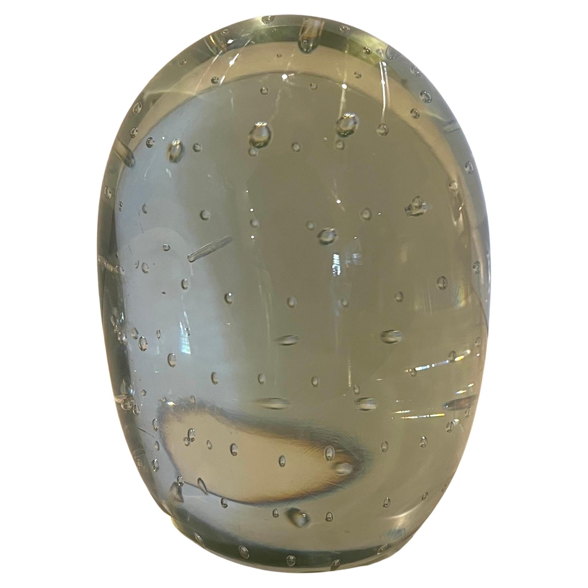 Clear glass single glass egg shaped bookend with intentional bubble pattern flat on one side to press on the books solid and heavy.