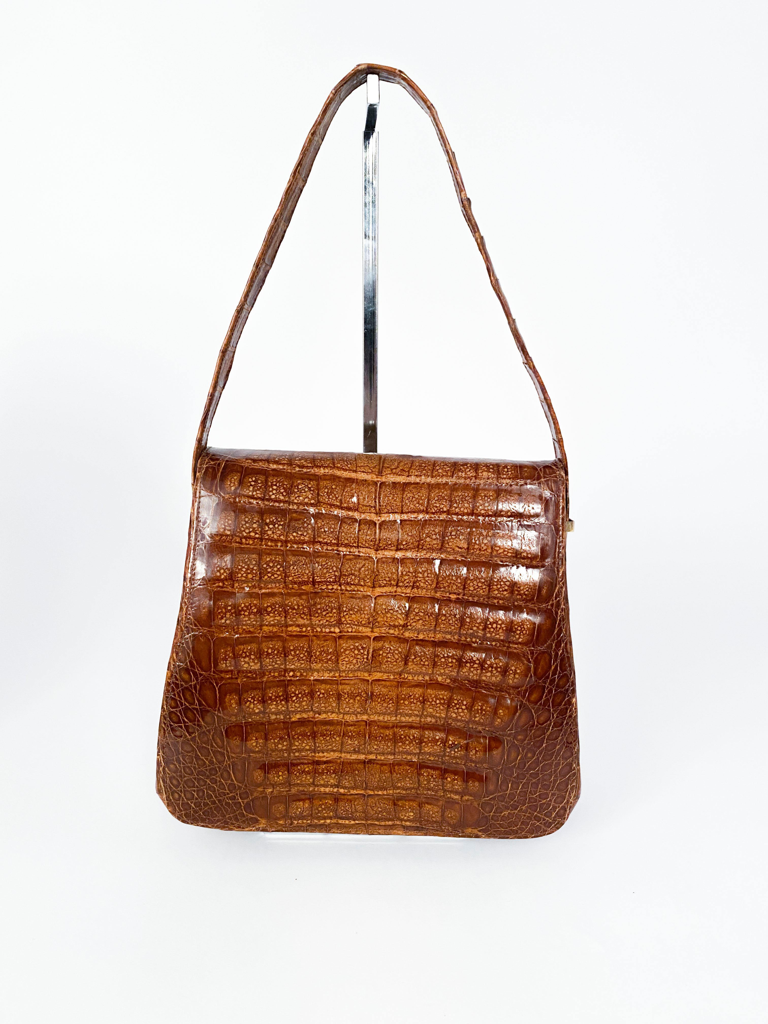 1980s light brown crocodile hand bag featuring a decorative and functional brass closure. The handle to this bag have fastenings that allows the handle to be extended about 3 inches on each side.