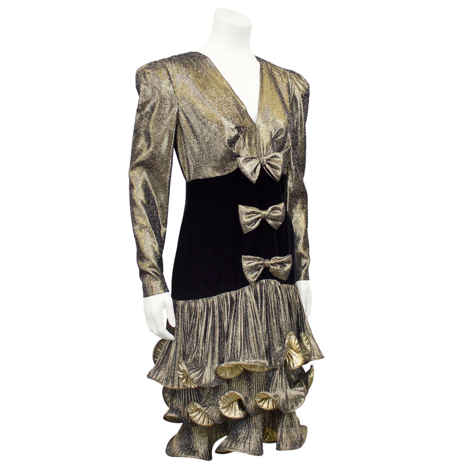 The ultimate 1980s cocktail/party dress by CSandra. Spotted gold lamé sleeves, bust and skirt with contrasting black velvet bodice with a drop waist. Long sleeves with strong shoulder pads and a v neckline. Three matching gold lamé bows down centre