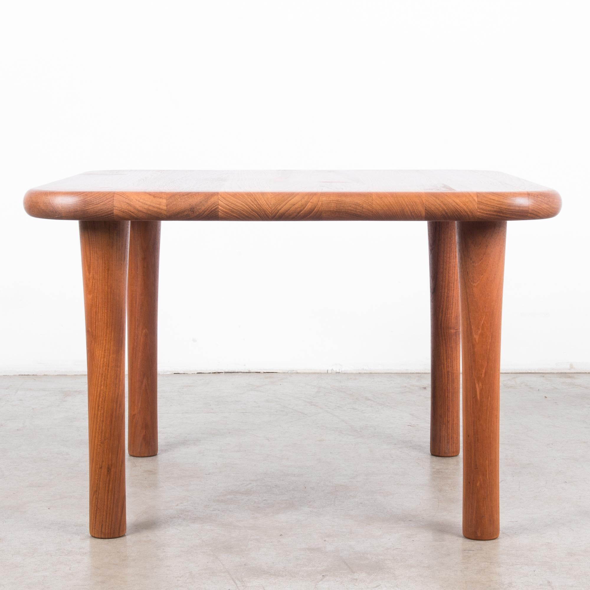 A wooden coffee table from Denmark, circa 1980. A square tabletop rests upon four cylindrical legs, which taper inwards only to flare out at the feet, giving the table a bold and distinctive posture. The corners of the tabletop are broad curves; the