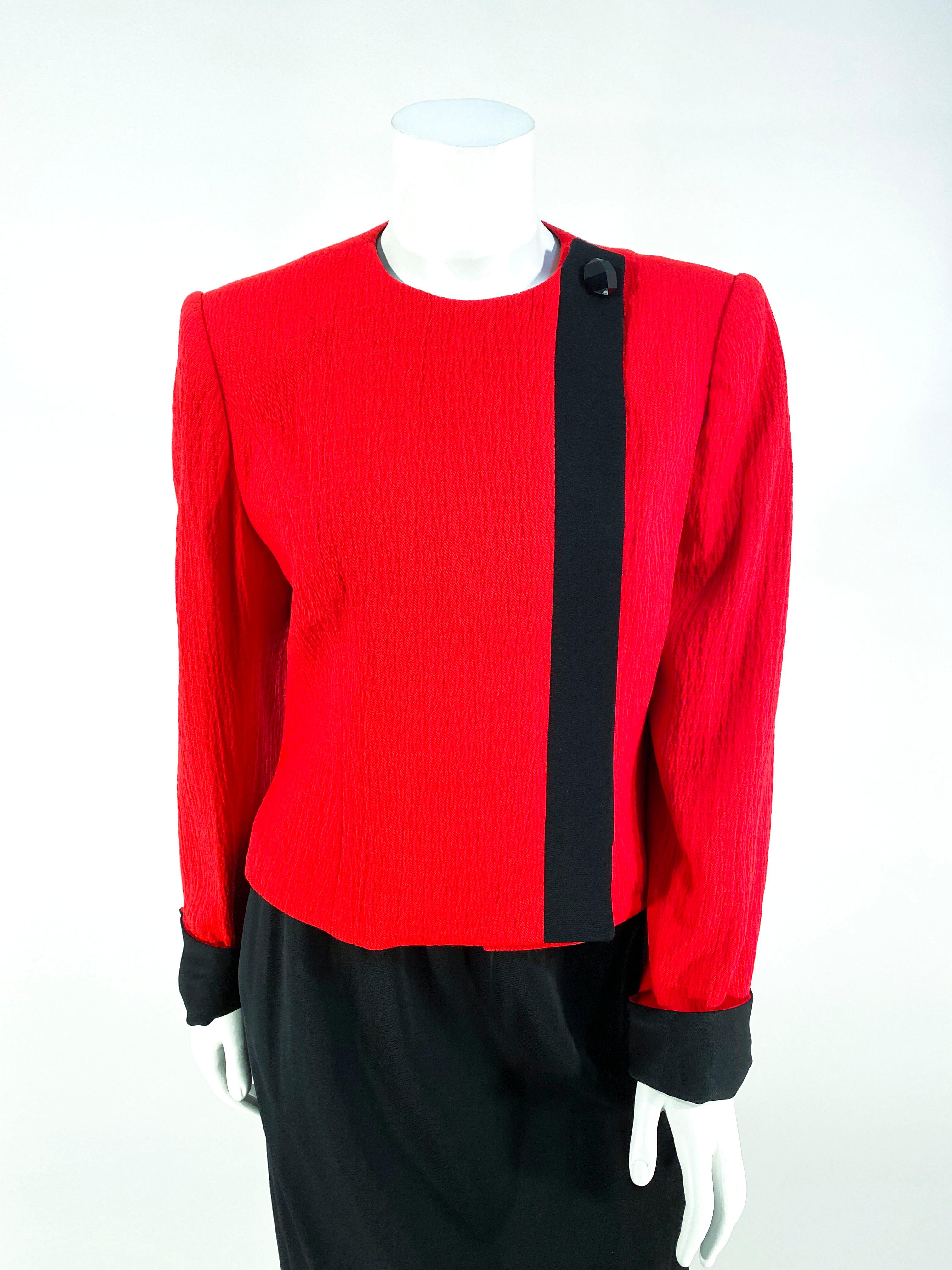 1980s David Hayes Red and black asymmetrical suit with front hidden front button closure, along a black boarder and decorative button at the neckline. The cuffs are rolled up with the matching black twill. The straight skirt is black with an applied