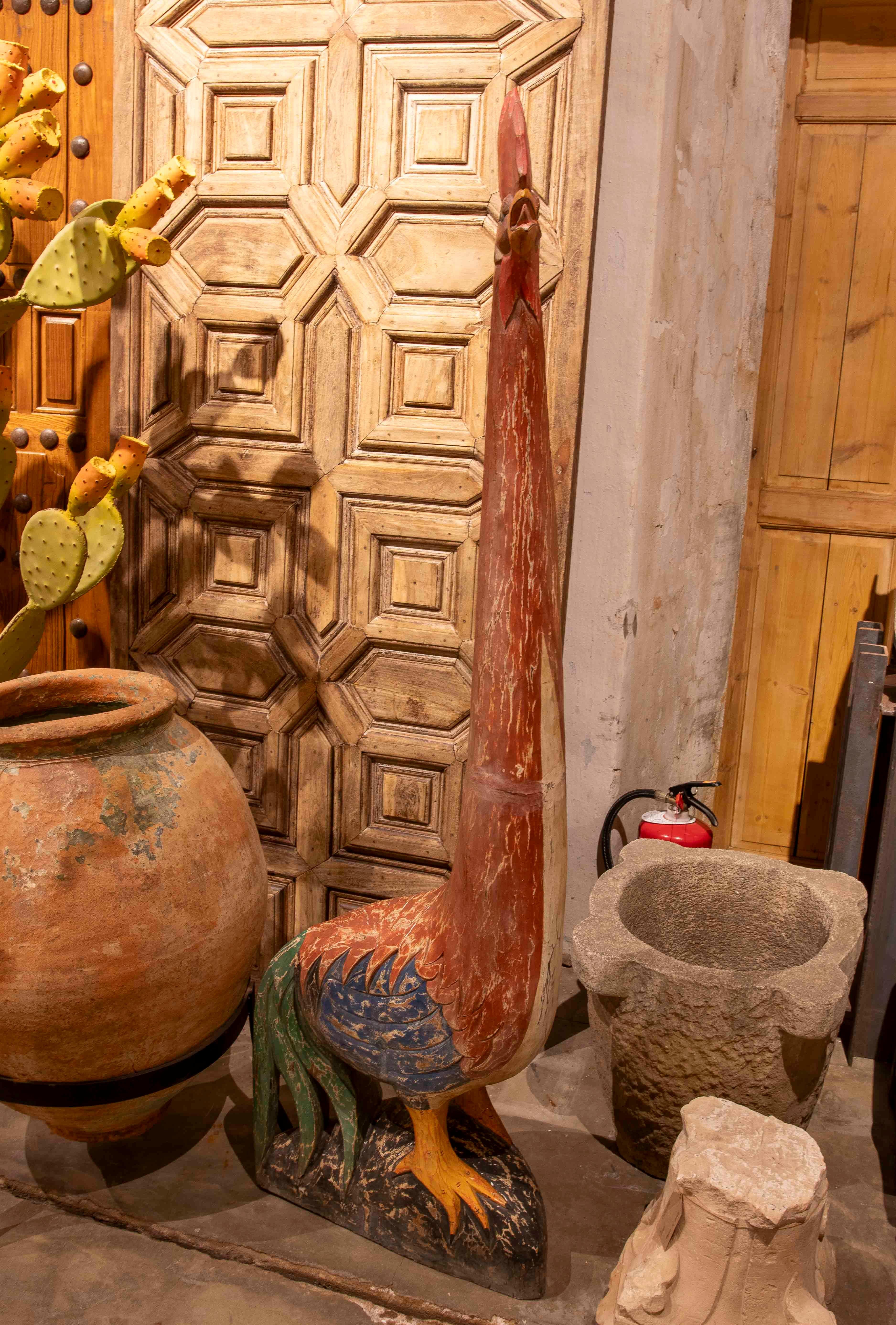 A rooster sculpture carved in wood with an original polychrome finish, highlighting a stylized and expressive design. Its imposing height and aged colors make it a unique decorative piece, ideal for rustic or eclectic spaces or folk art collections.