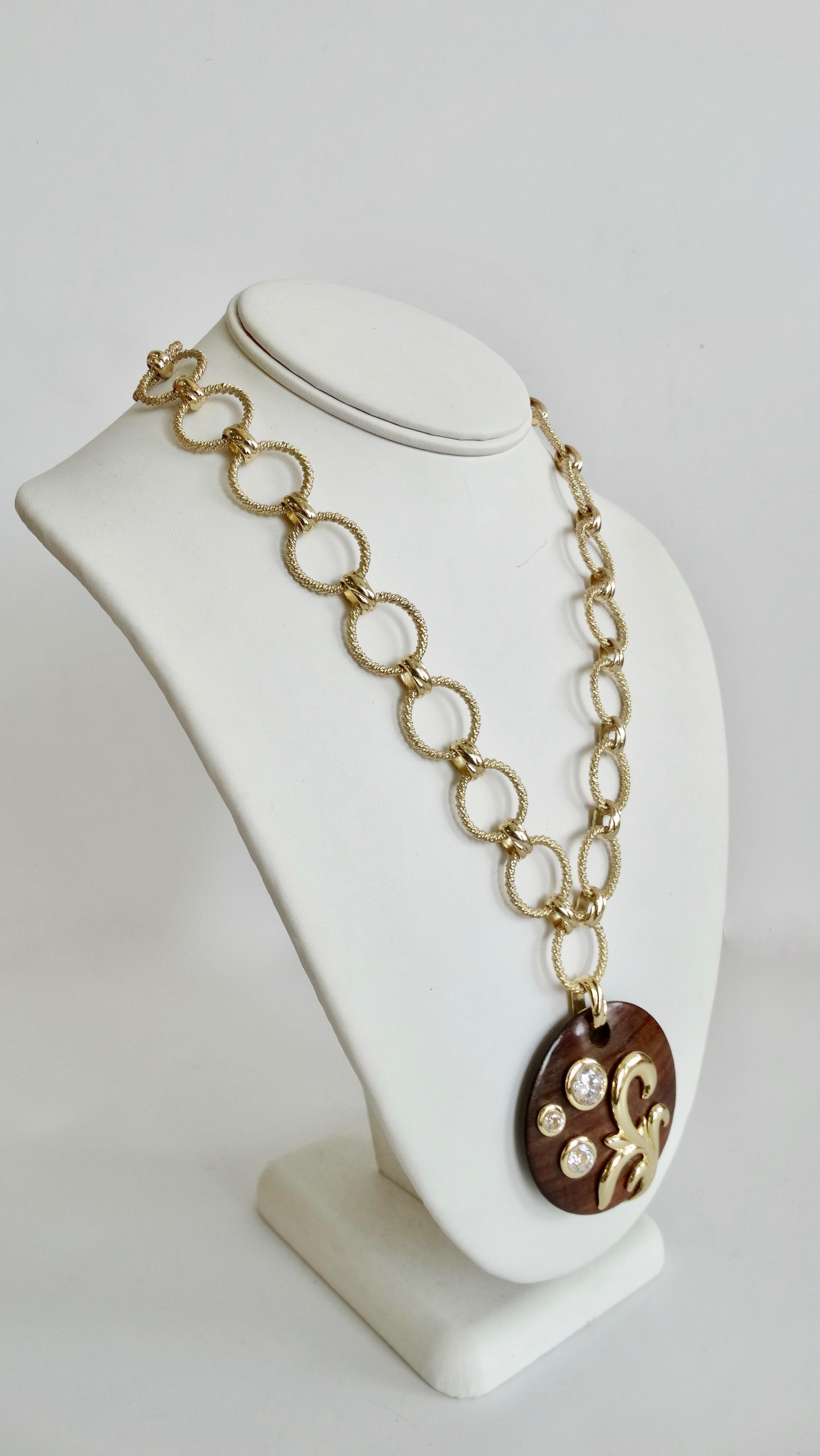 We all need a great vintage jewelry piece in our collection! Circa late 1980s, this Dominique Aurientis necklace features a textured gold plated link chain and a round dark wood stained pendant embellished with three Swarovski crystals and a gold