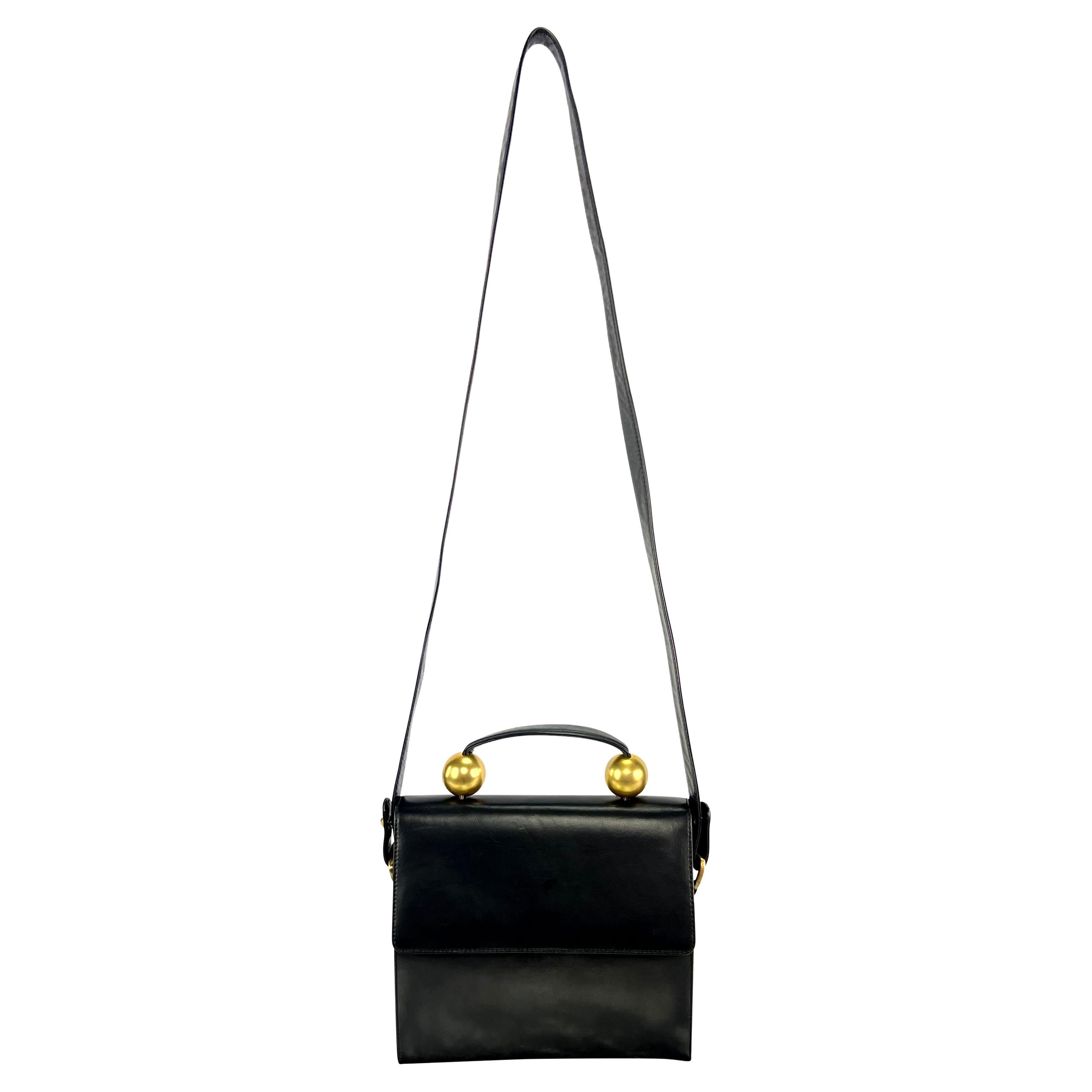 De finales de los años 80, este bolso de asa superior de piel negra de Donna Karan presenta un cierre de solapa y esferas doradas en la base del asa. Completado con una correa para el hombro, este elegante bolso es el accesorio de lujo más