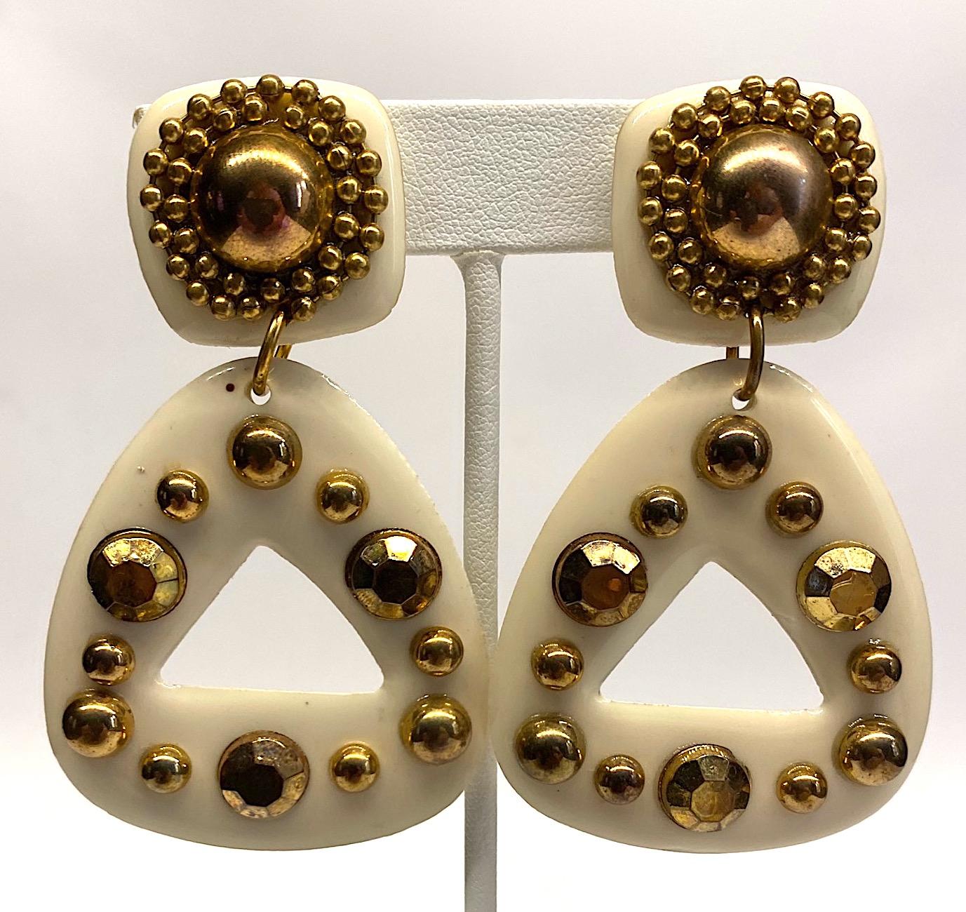 A very stylish pair of off white / cream resin or plastic earrings from the 1980s. The earrings are accented with applied gold tone studs and gold flat back crystals. The top piece with clip back is 1 inch square. The bottom triangular pendant is