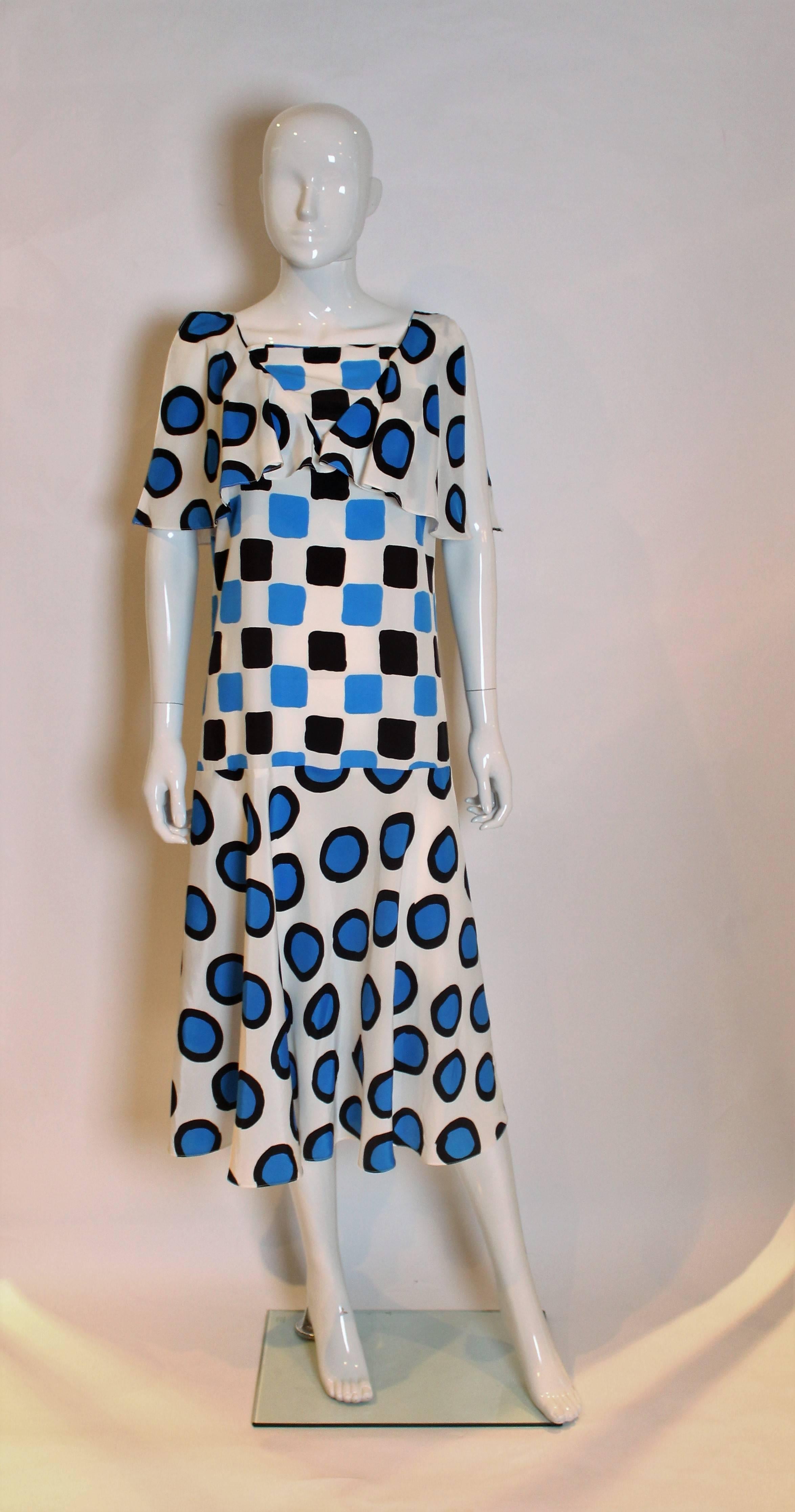 A chic silk mix dress by Christina Strambolia ( who produced the Diana revenge dress). The dress has a white background, with blue and black circles, drop waist, flared skirt and loose collar.