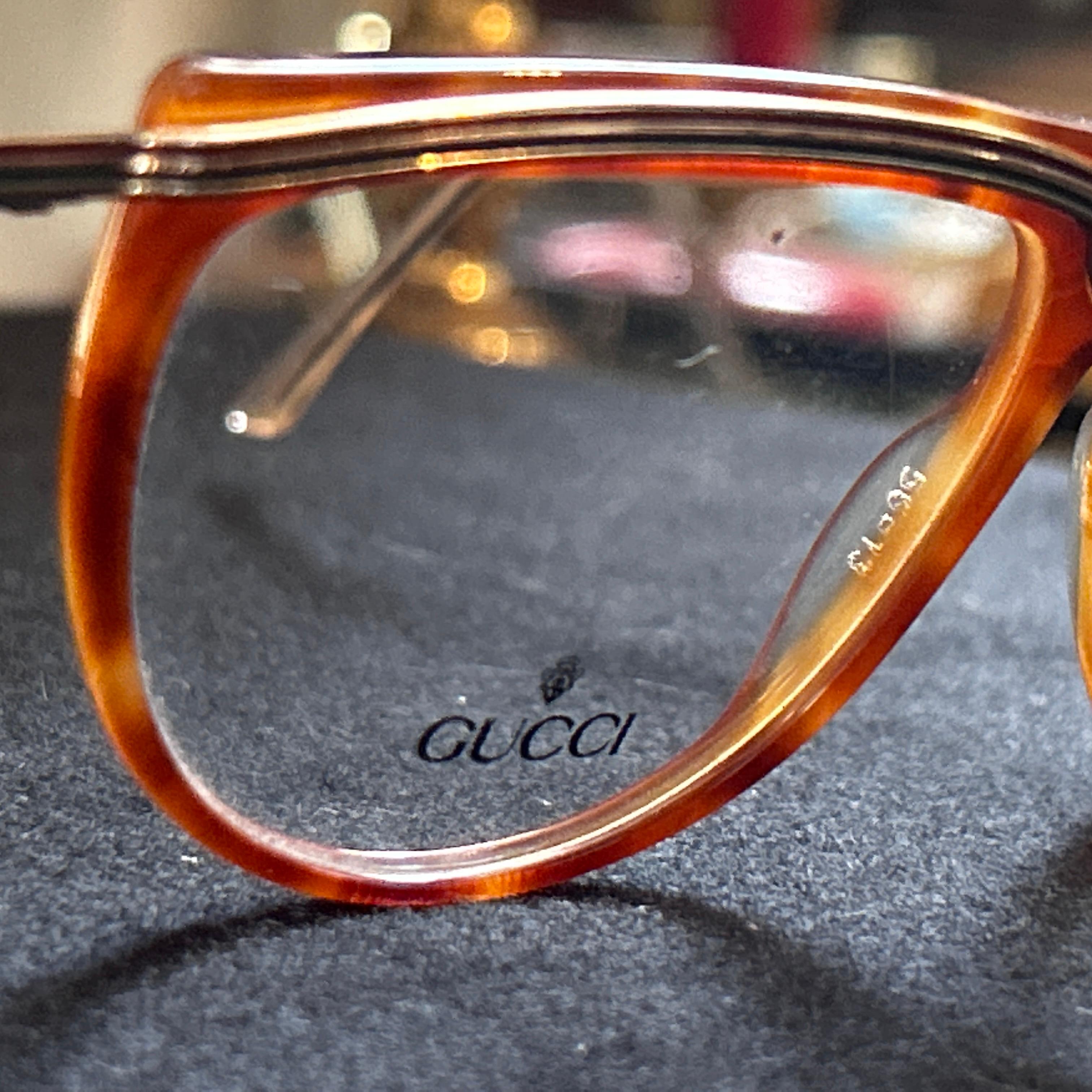 These sunglasses are a classic example of 1980s vintage luxury fashion by Gucci. They have a bold frame design featuring a faux tortoiseshell pattern, which gives the appearance of rich, mottled browns and amber tones. The frame shape is