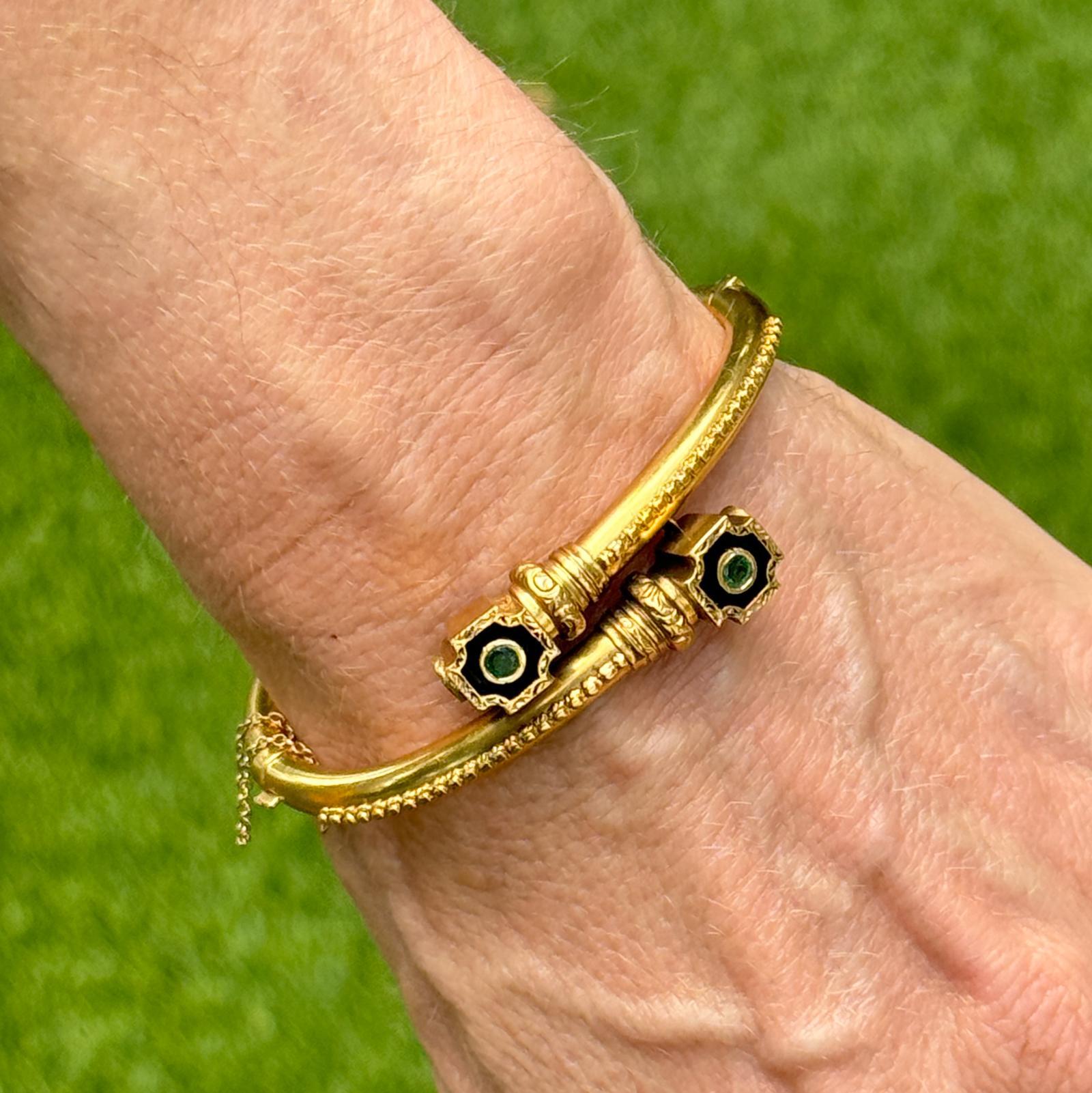 Ein eleganter Bypass-Armreif aus 14-karätigem Gelbgold mit zwei leuchtenden, runden Smaragden vor einem Hintergrund aus schlichter schwarzer Emaille. Der auffällige Kontrast zwischen den tiefgrünen Smaragden und der reichen Emaille unterstreicht das