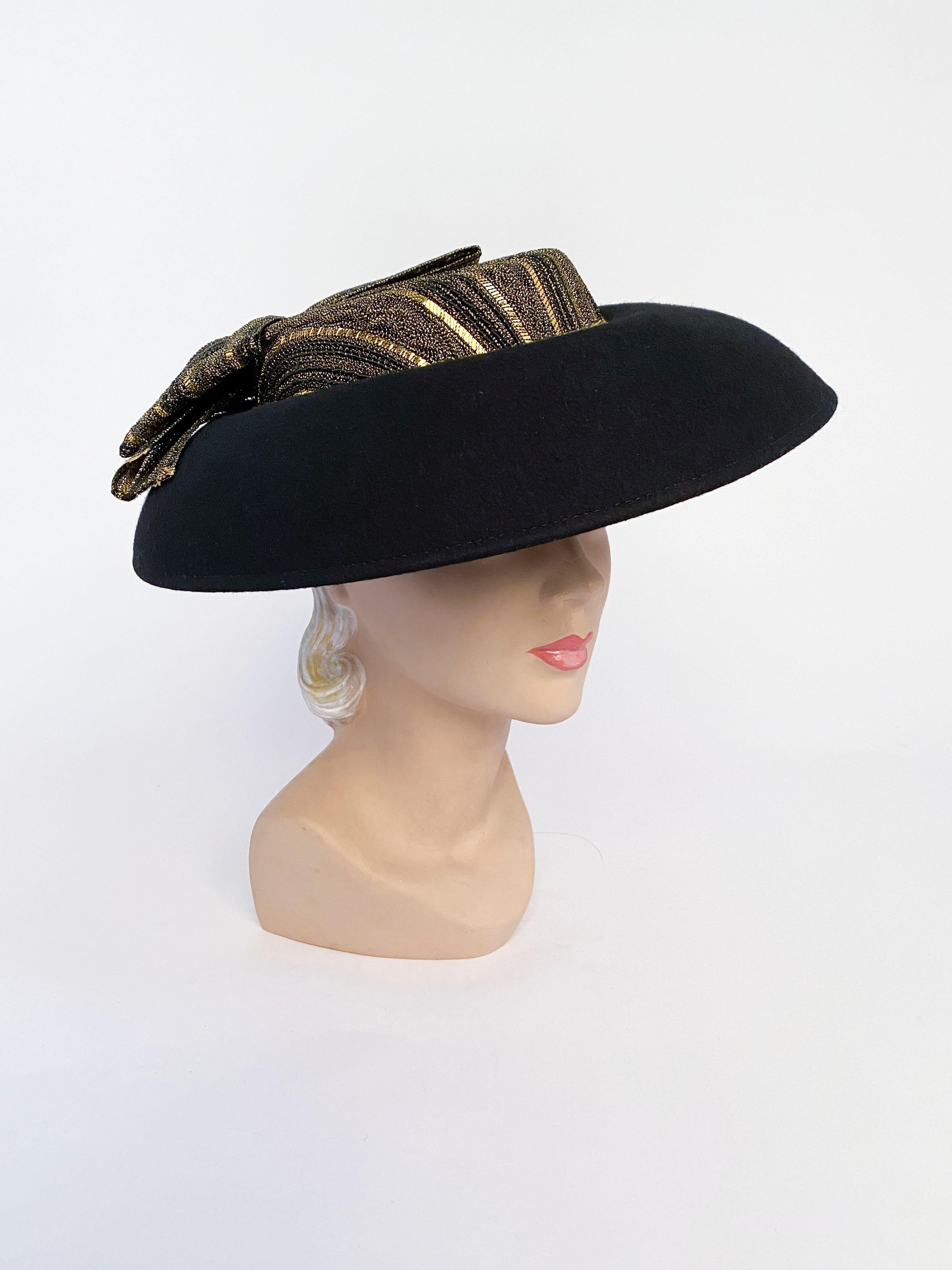 1980s Eric Javits black wool felt wide brimmed picture hat with a shallow crown decorated with a multi-textured gold lurex textile that matches the enlarged bow that decorates the back.