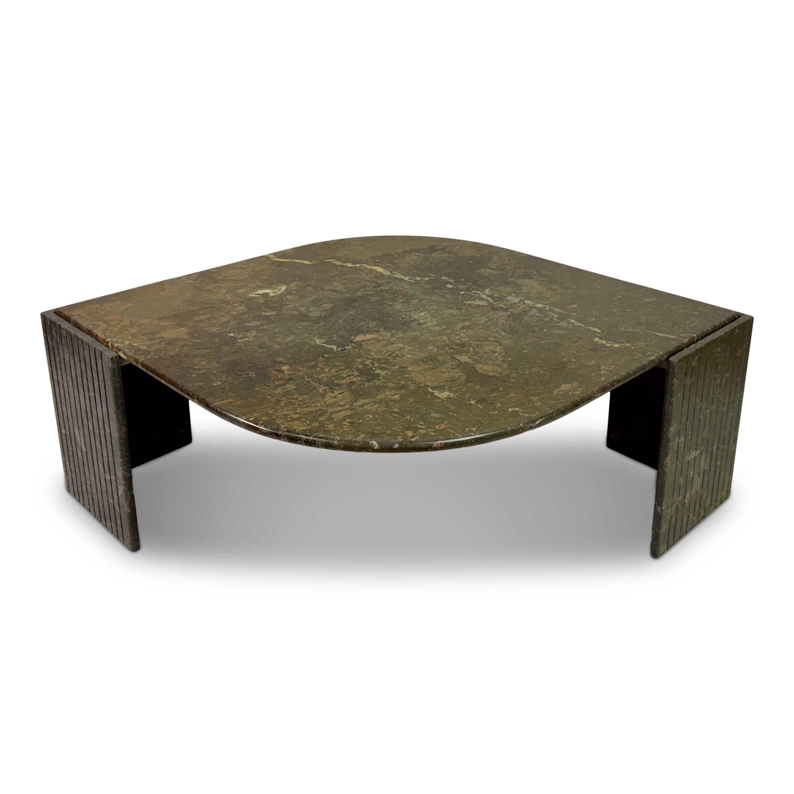 This table features a low, eye-shaped design with a distinctive, curved marble top. The surface of the table has a mottled, earthy texture with shades of brown, green, and hints of other natural colours, giving it a rugged and organic appearance.