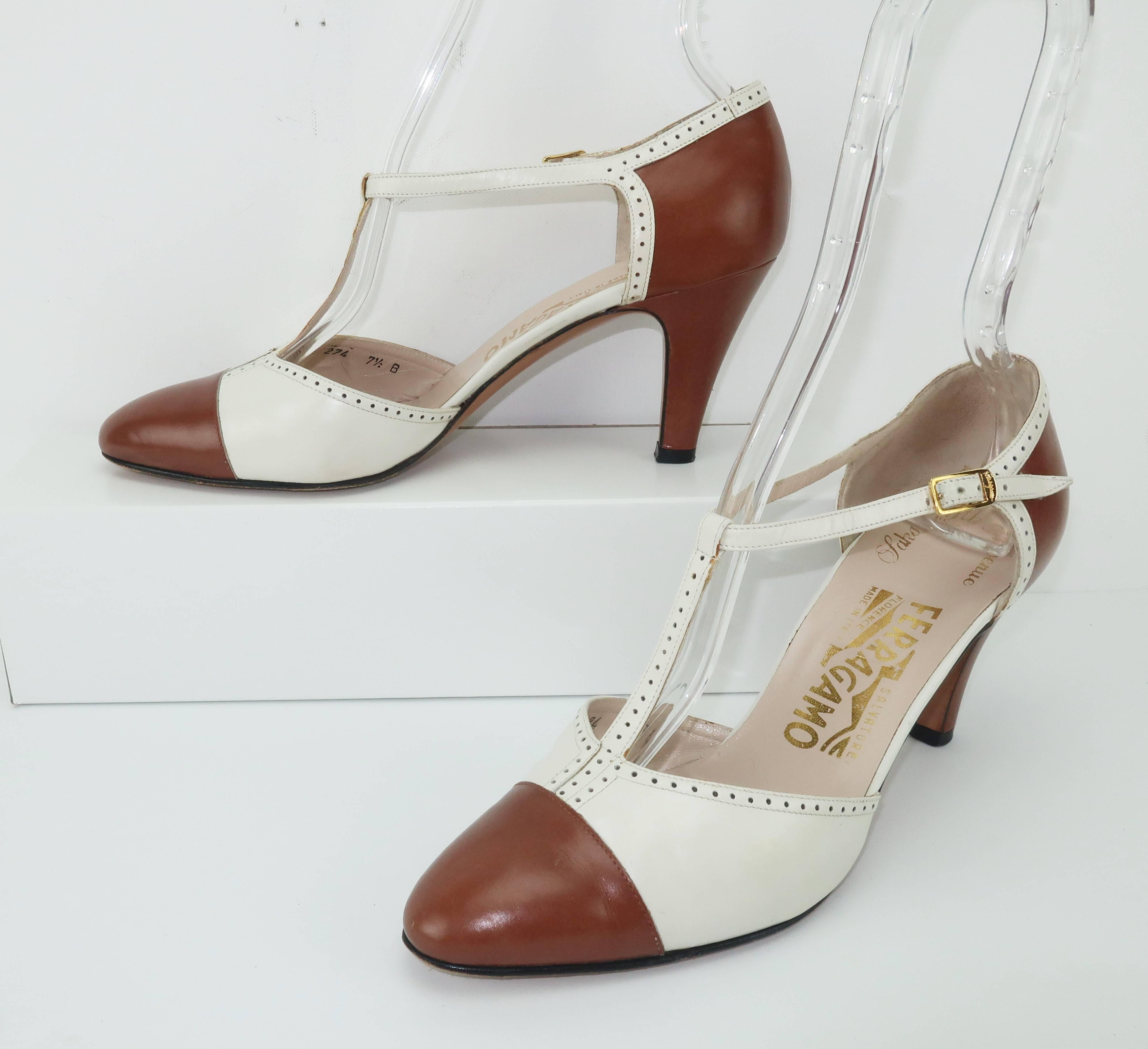 Ferragamo creates a classic spectator pump with a nod to the 1920's and 1930's t-strap silhouette from a two tone leather design in shades of versatile camel and ivory white.  The shoes feature a gold tone logo buckle at the side offering